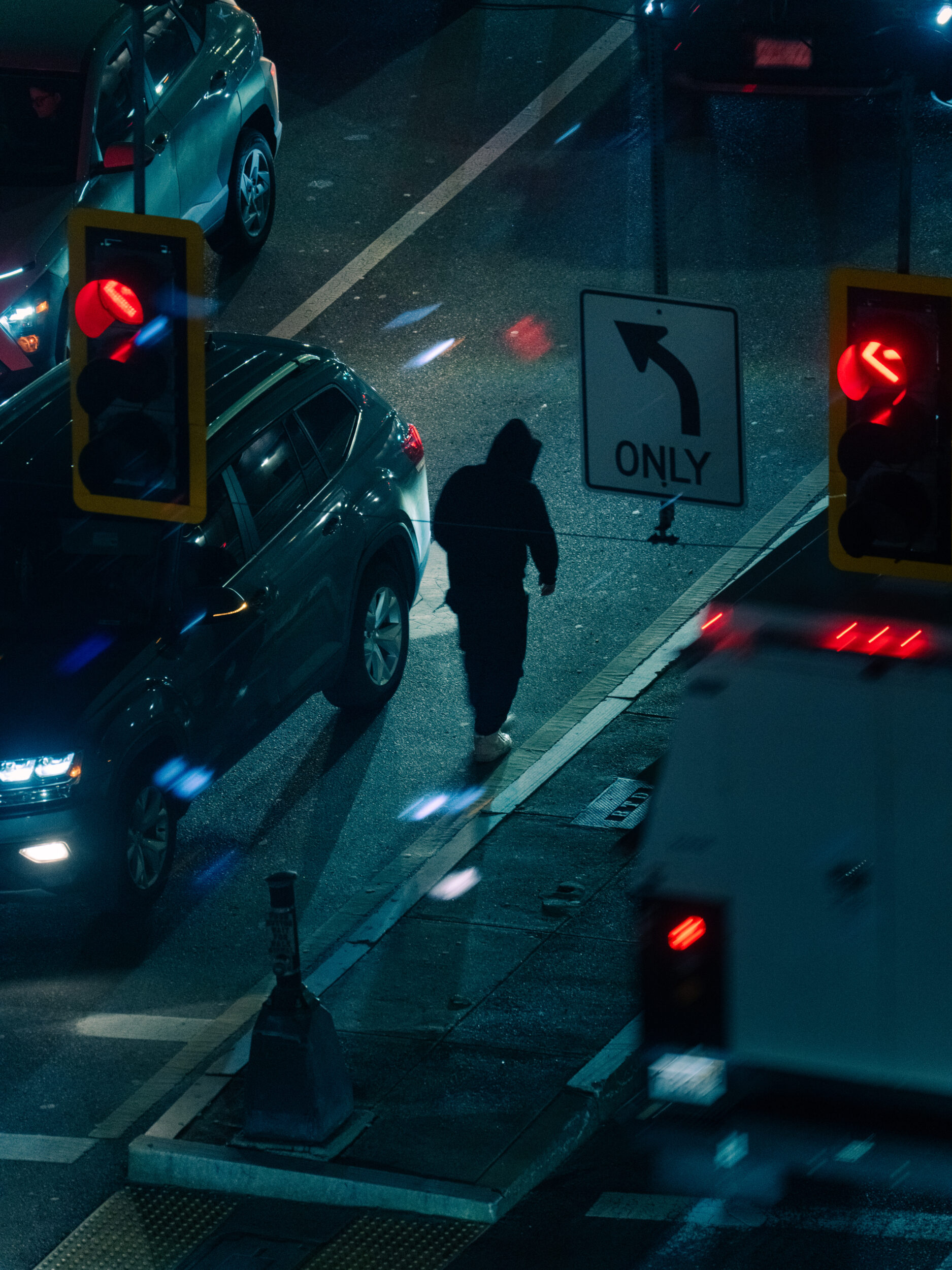A silhouetted figure walks between cars and red traffic lights at night near Mass and Cass in Boston