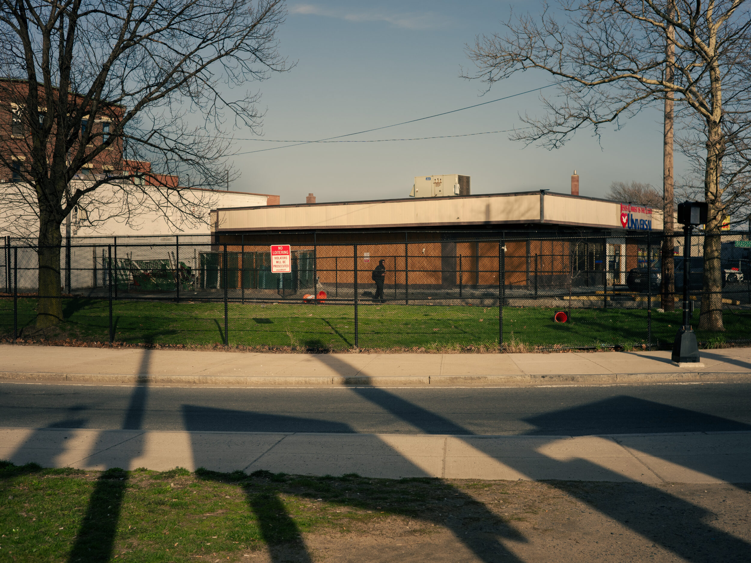 A boarded-up building surrounded by chain-link fence and a No Loitering sign near Mass and Cass in Boston