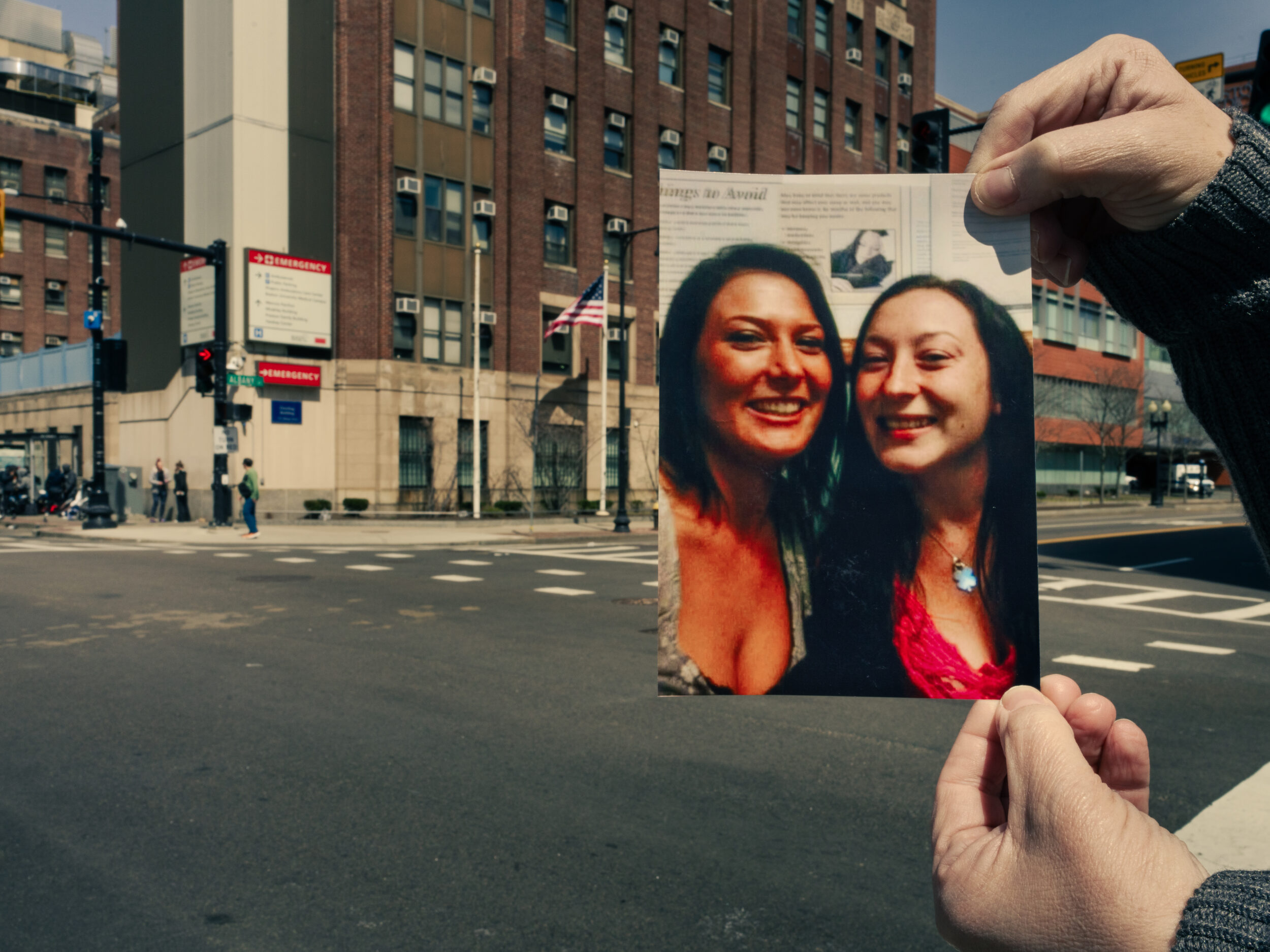A photograph of twin sisters Courtney and Kerri Flynn is held up near Massachusetts Avenue with BMC in the background