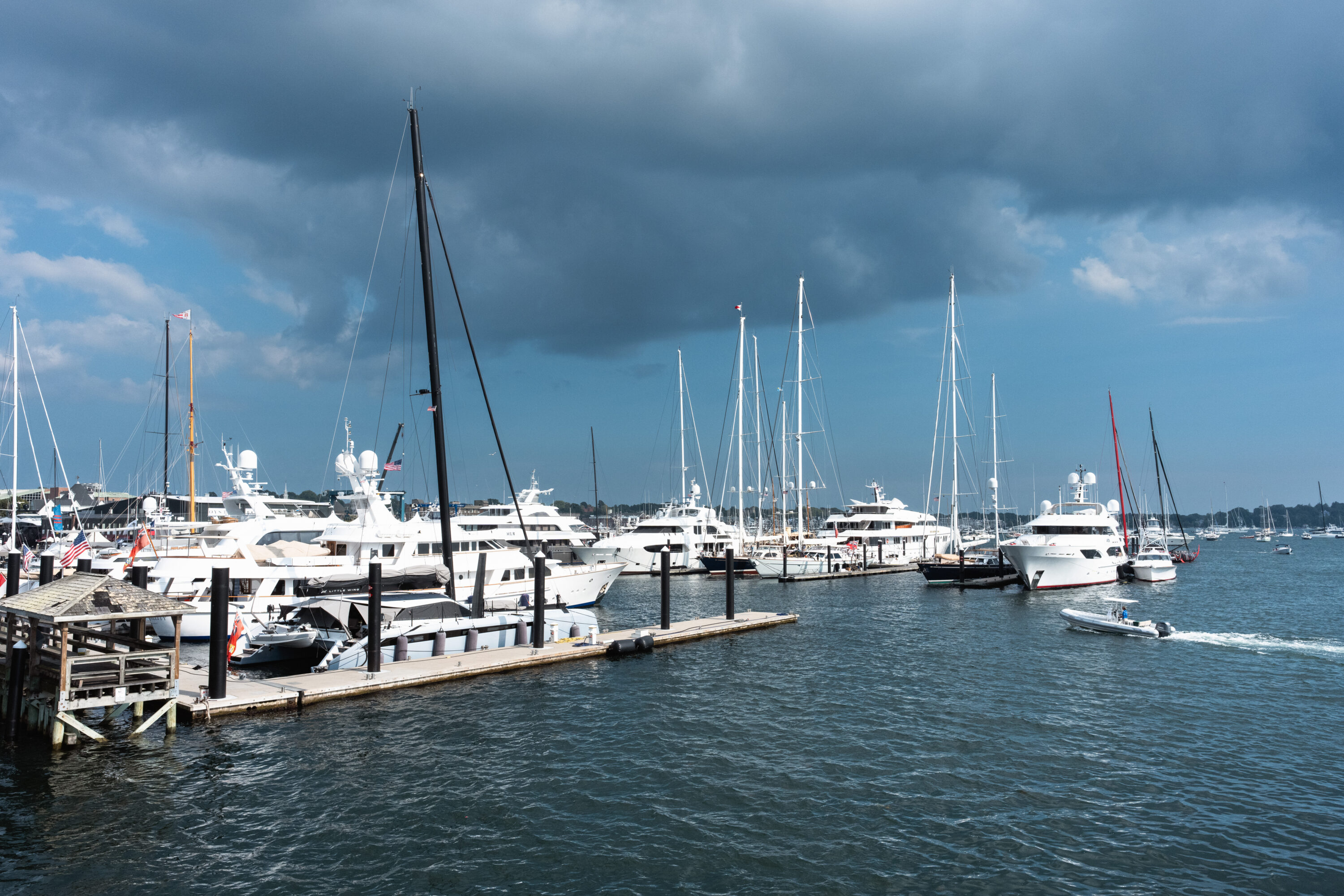 A small motorboat leaves a curved wake beside rows of yachts beneath dark clouds.