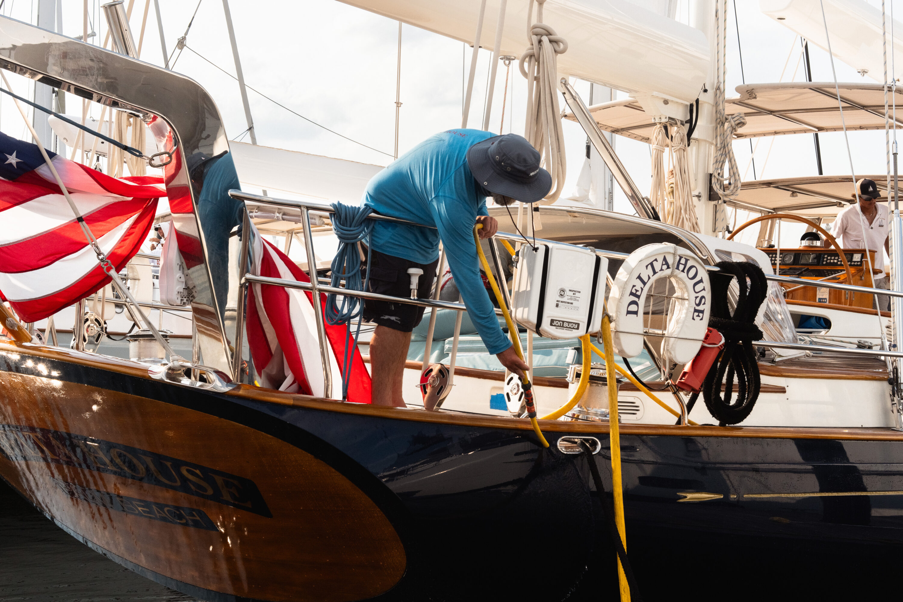 A person in a blue shirt leans over the stern of Delta House with a yellow hose.