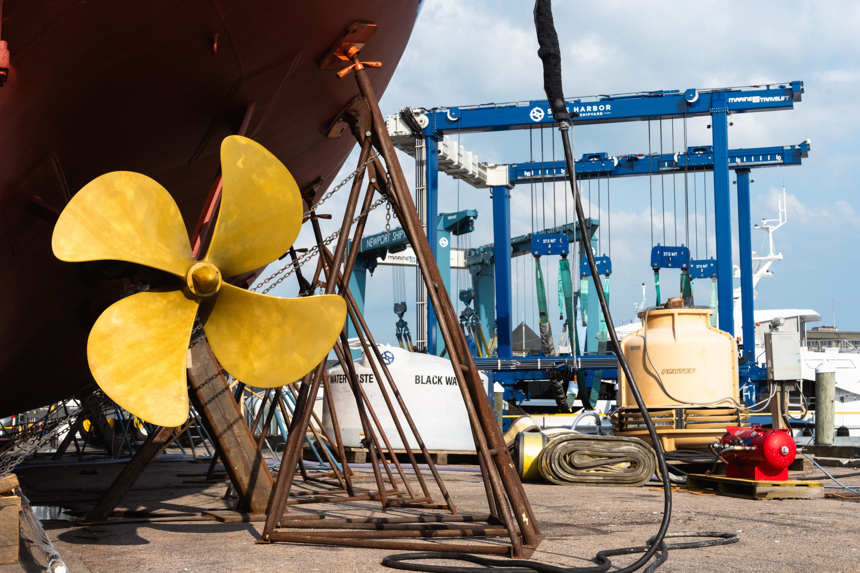 A golden propeller fills the foreground beneath a red hull, with a blue boat lift behind it.