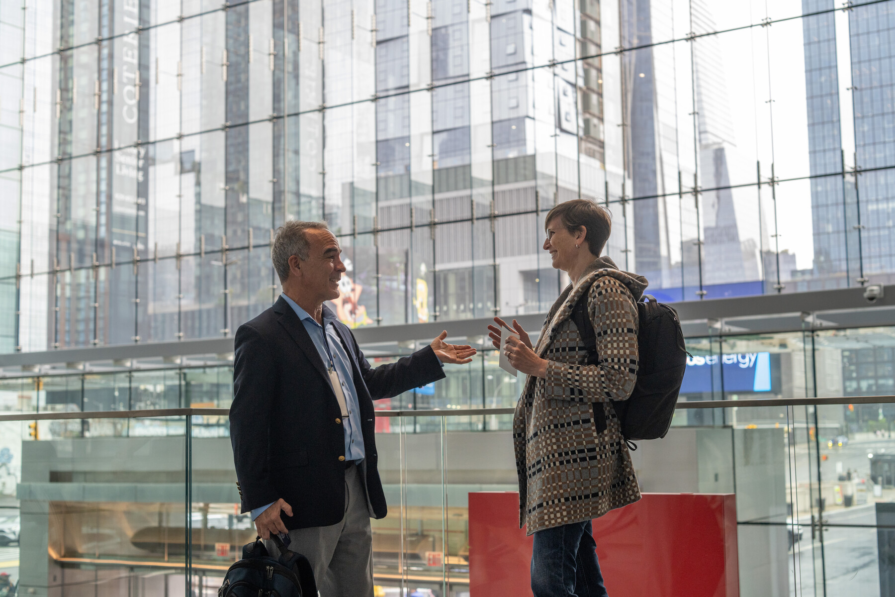 Two people talk beside a glass wall overlooking Manhattan.