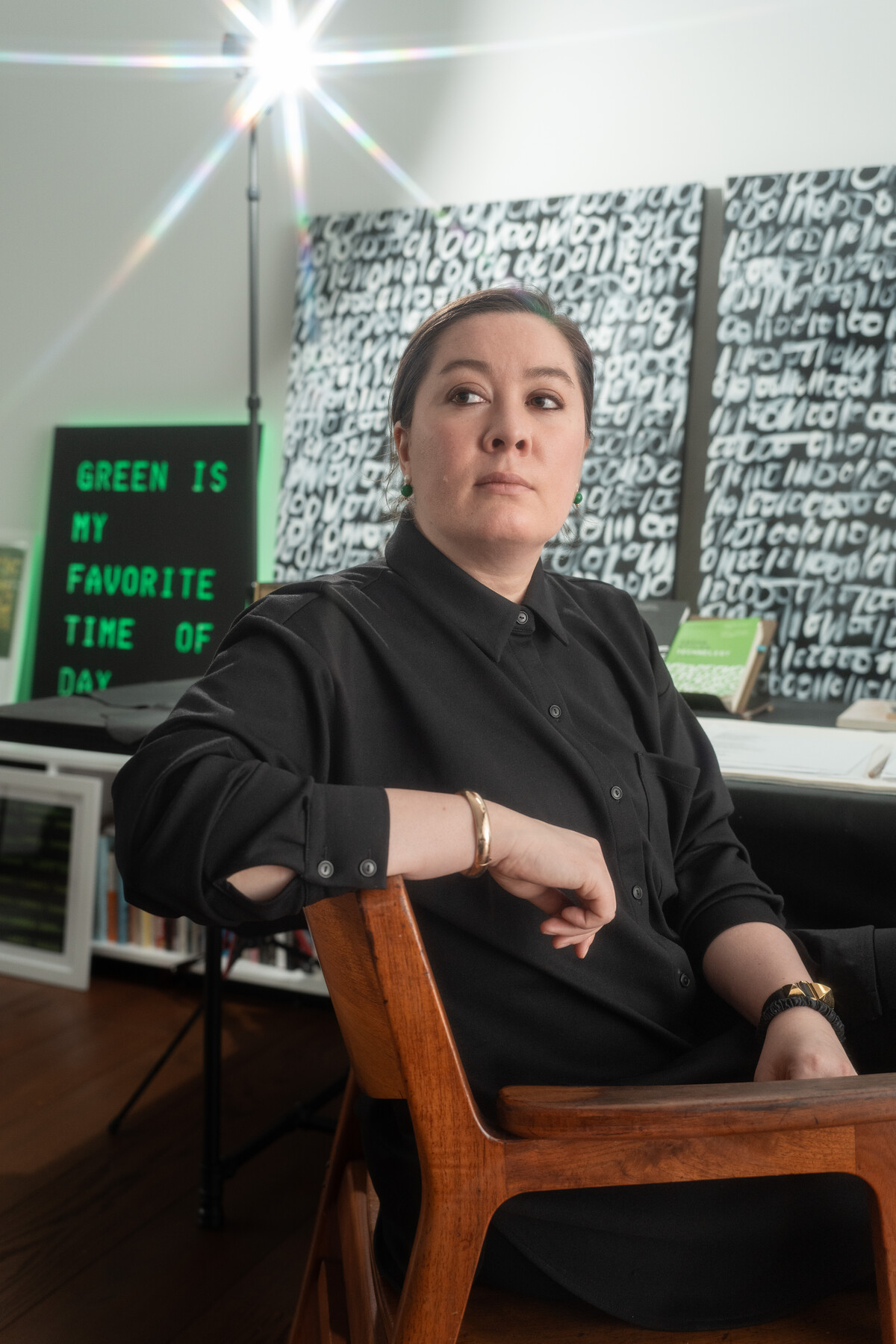 Sasha Stiles sits in her studio before a green text display and a wall of black and white lettering.