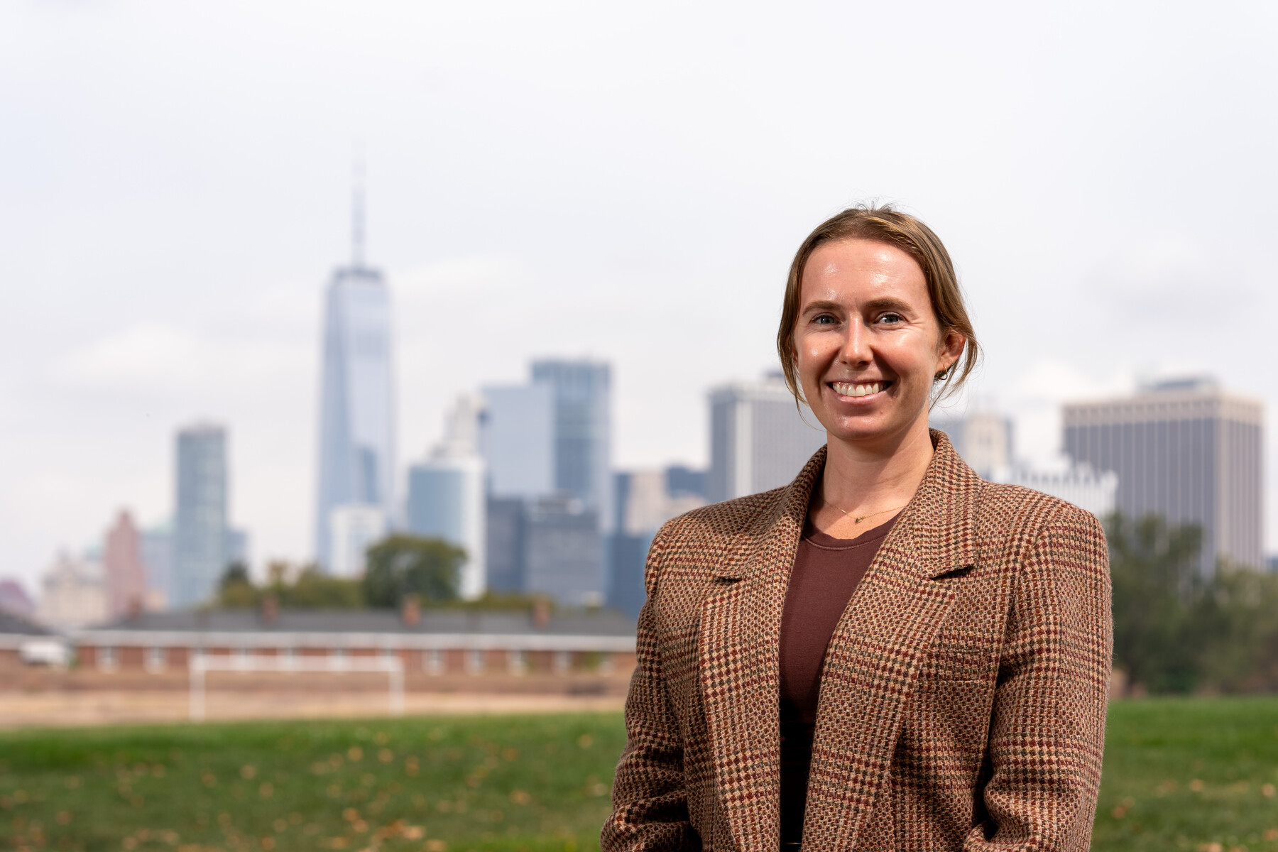 A woman poses on Governors Island with the Manhattan skyline behind her.