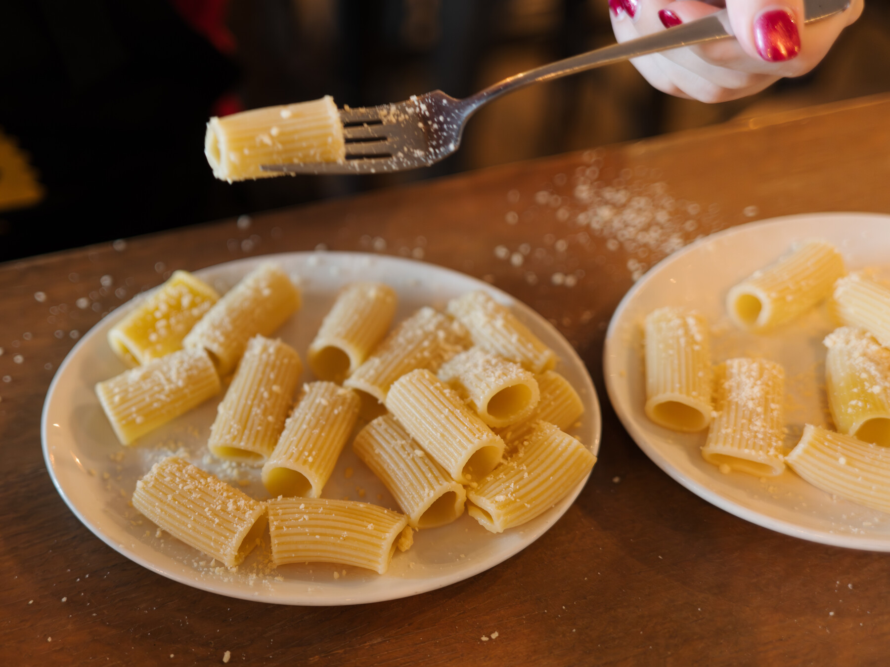 A fork lifts a piece of pasta over two plates of rigatoni.