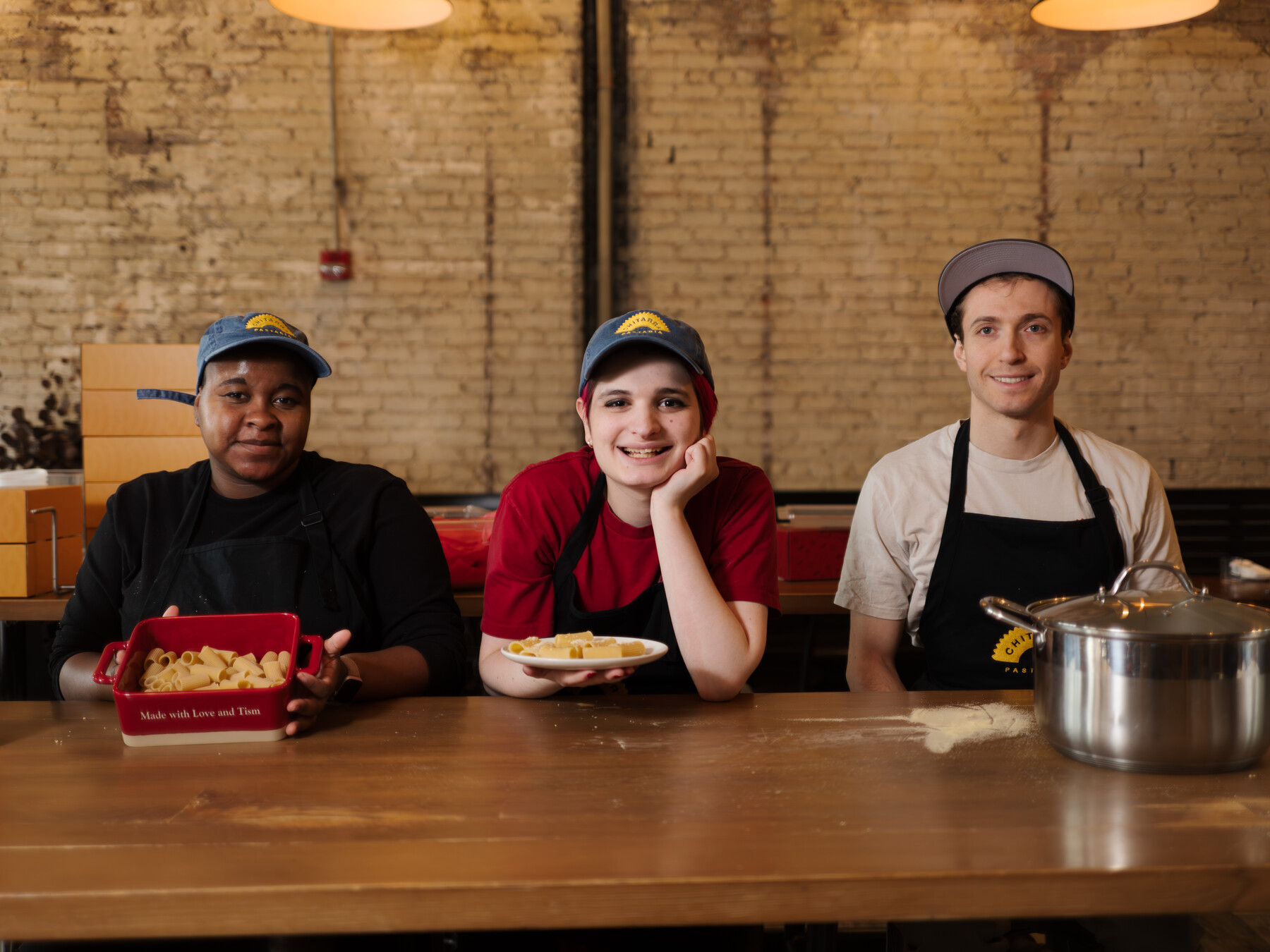 Ezra Kukis, Julia Agostino and Stefano Micali sit together behind pasta, a plate and a pot.