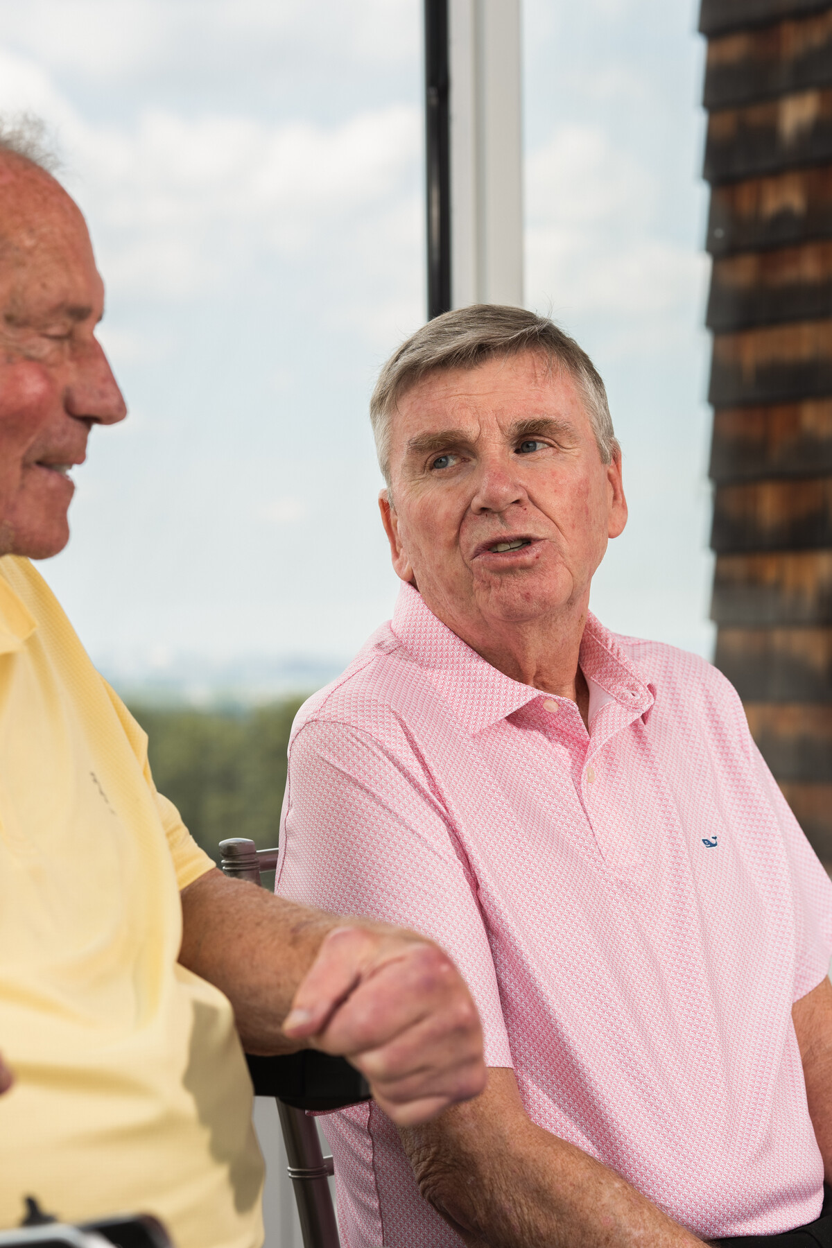 Mike Lynch in a pink shirt speaks while Bob Lobel, in yellow, sits beside him.