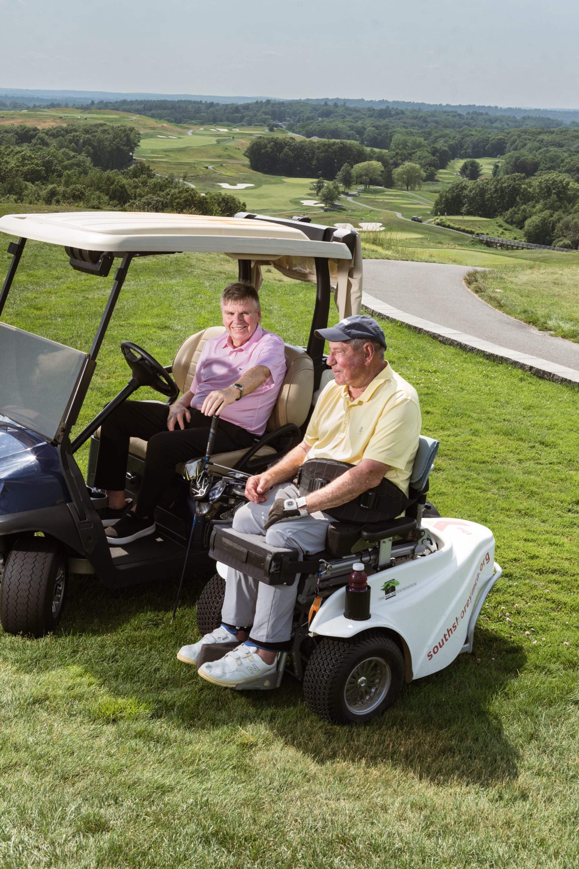 Mike Lynch and Bob Lobel sit beside each other on a grassy hillside overlooking the golf course at Granite Links.
