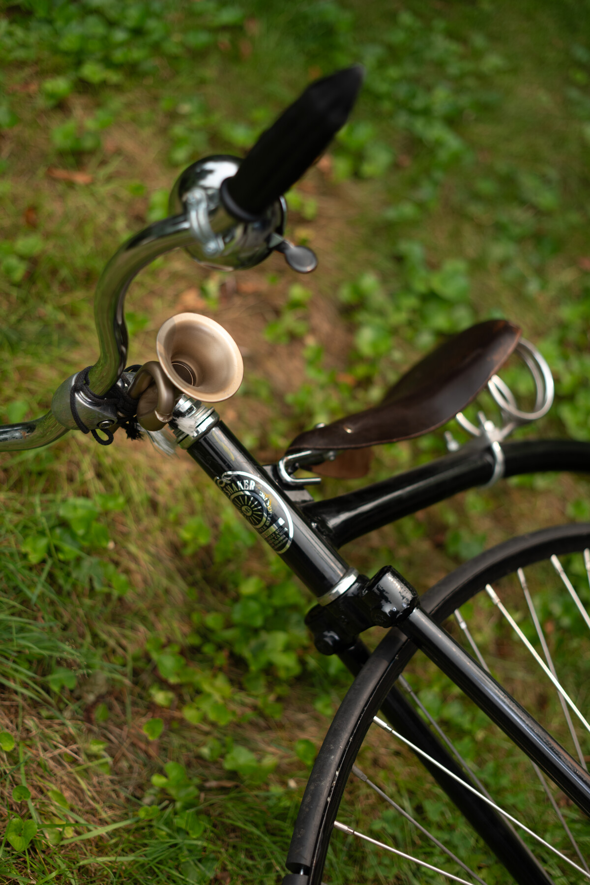 A small metal horn is fixed to the handlebars of a black bicycle.