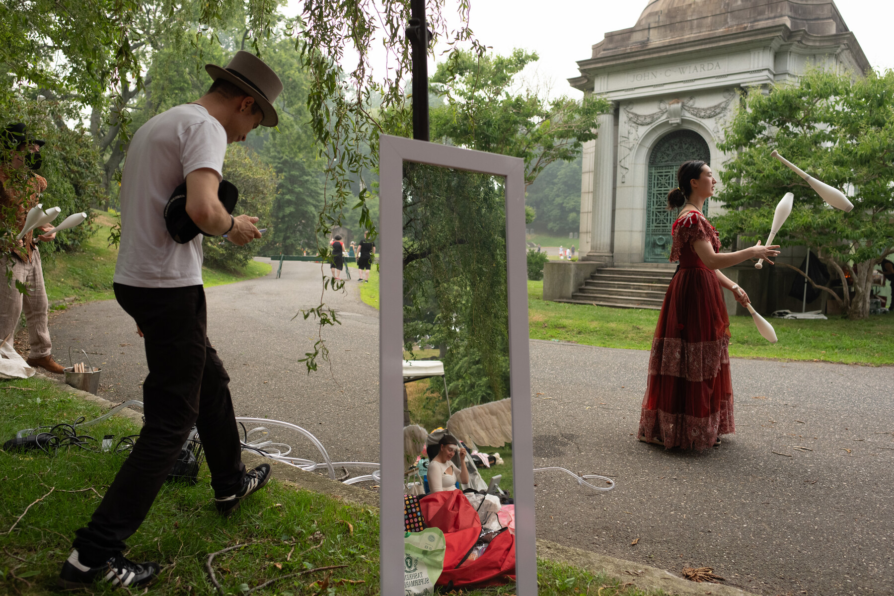 A performer rehearses near a standing mirror as a juggler practices by the mausoleum.
