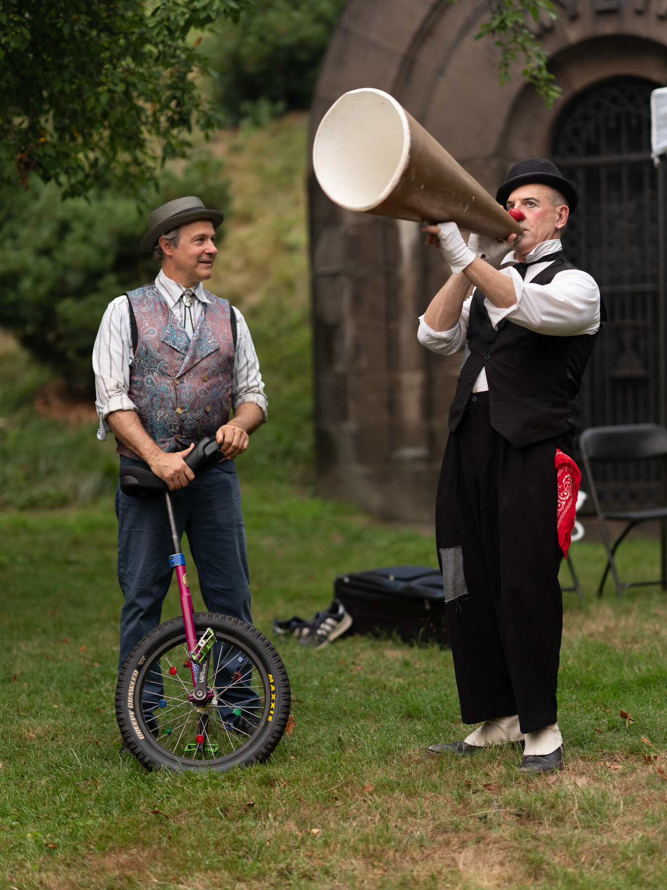 A bowler-hatted performer speaks through a megaphone beside a unicycle.