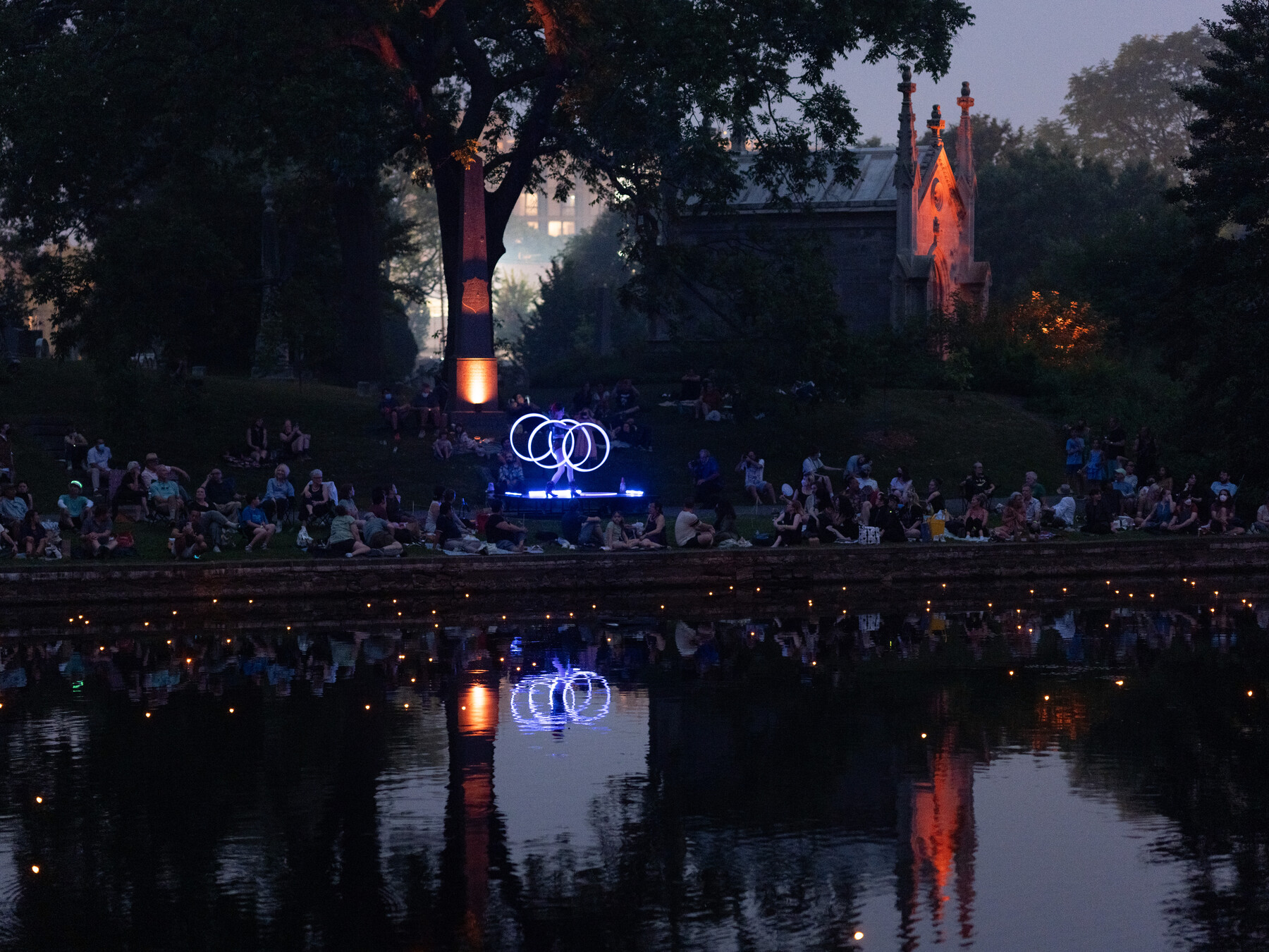 Crowds watch across Crescent Water as illuminated hoops glow below the lit Niblo mausoleum at night.