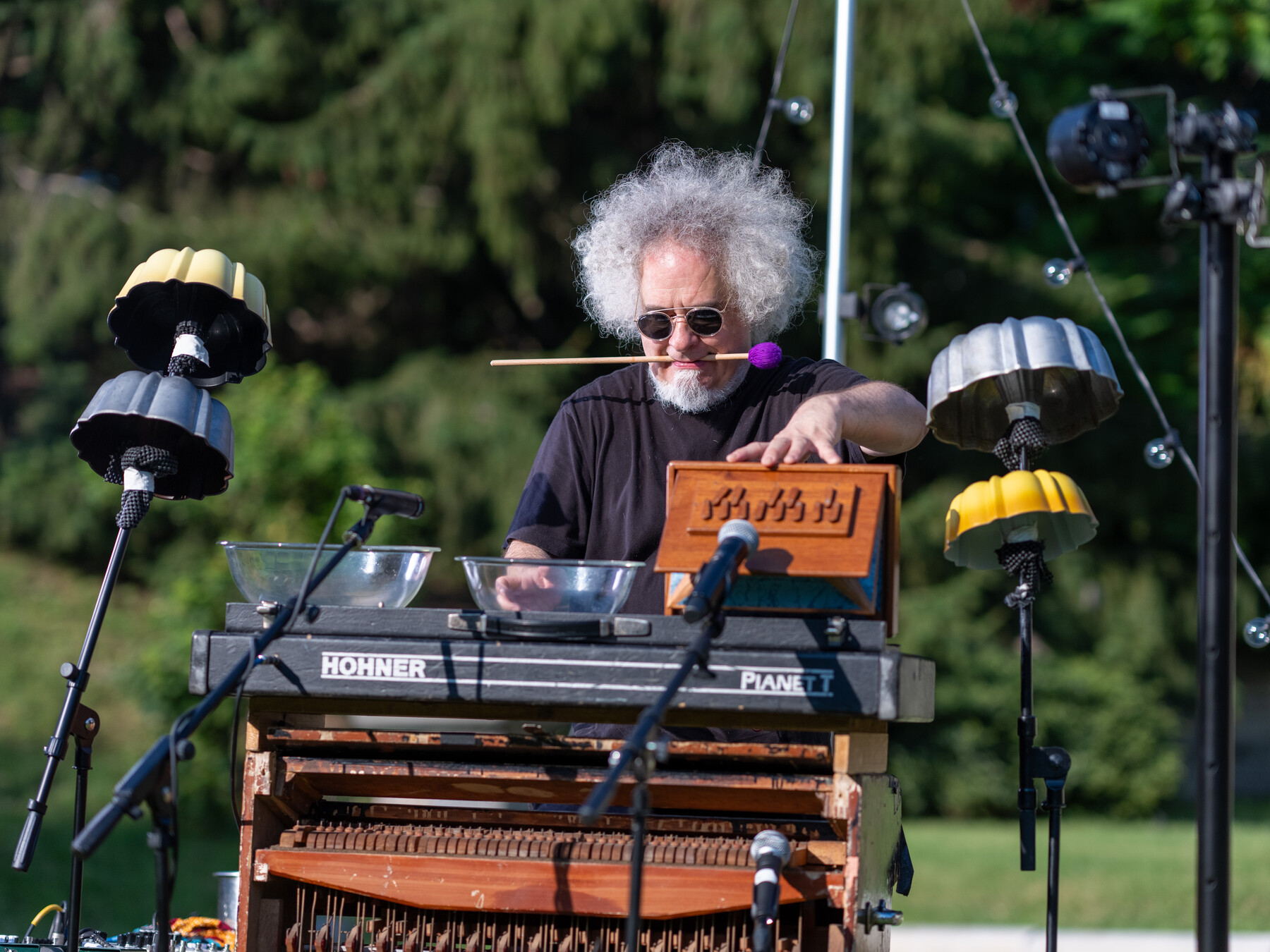 A gray-haired musician performs at a keyboard surrounded by percussion instruments.