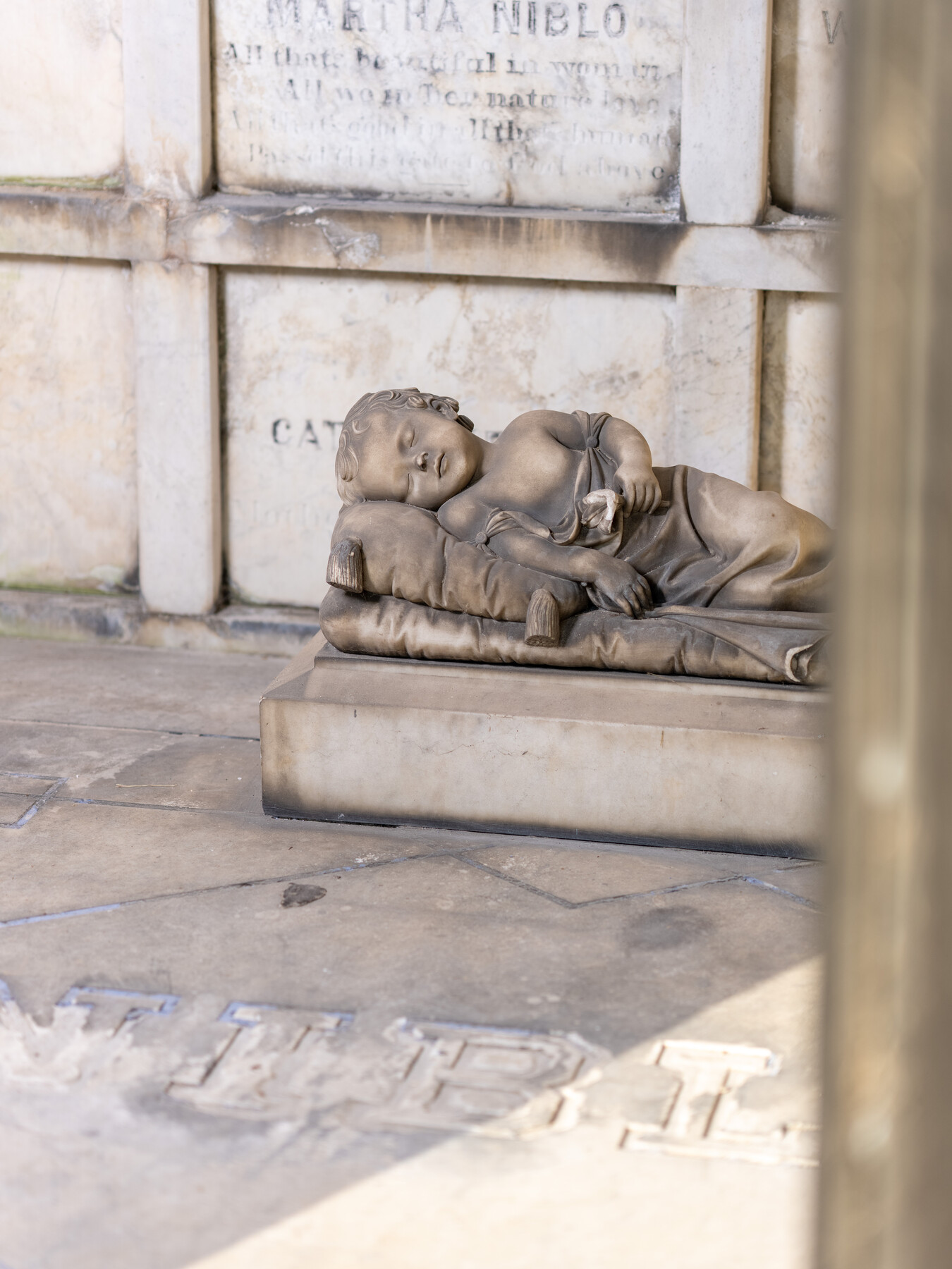 A sleeping child sculpture rests below the name Martha Niblo on a stone memorial.