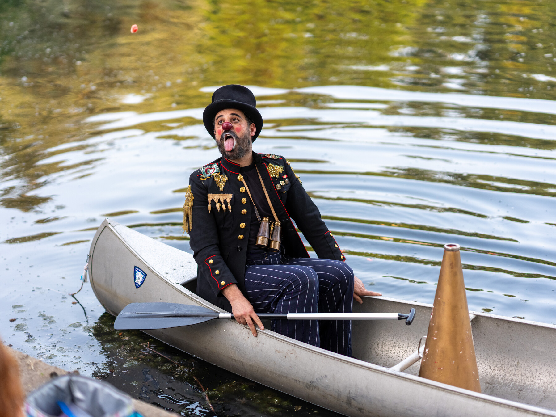 A bowler-hatted clown sits in a canoe at the edge of Crescent Water.
