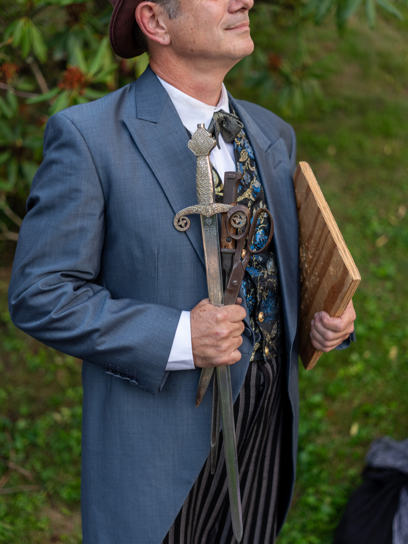 A performer in a blue jacket holds a sword and a small wooden case.