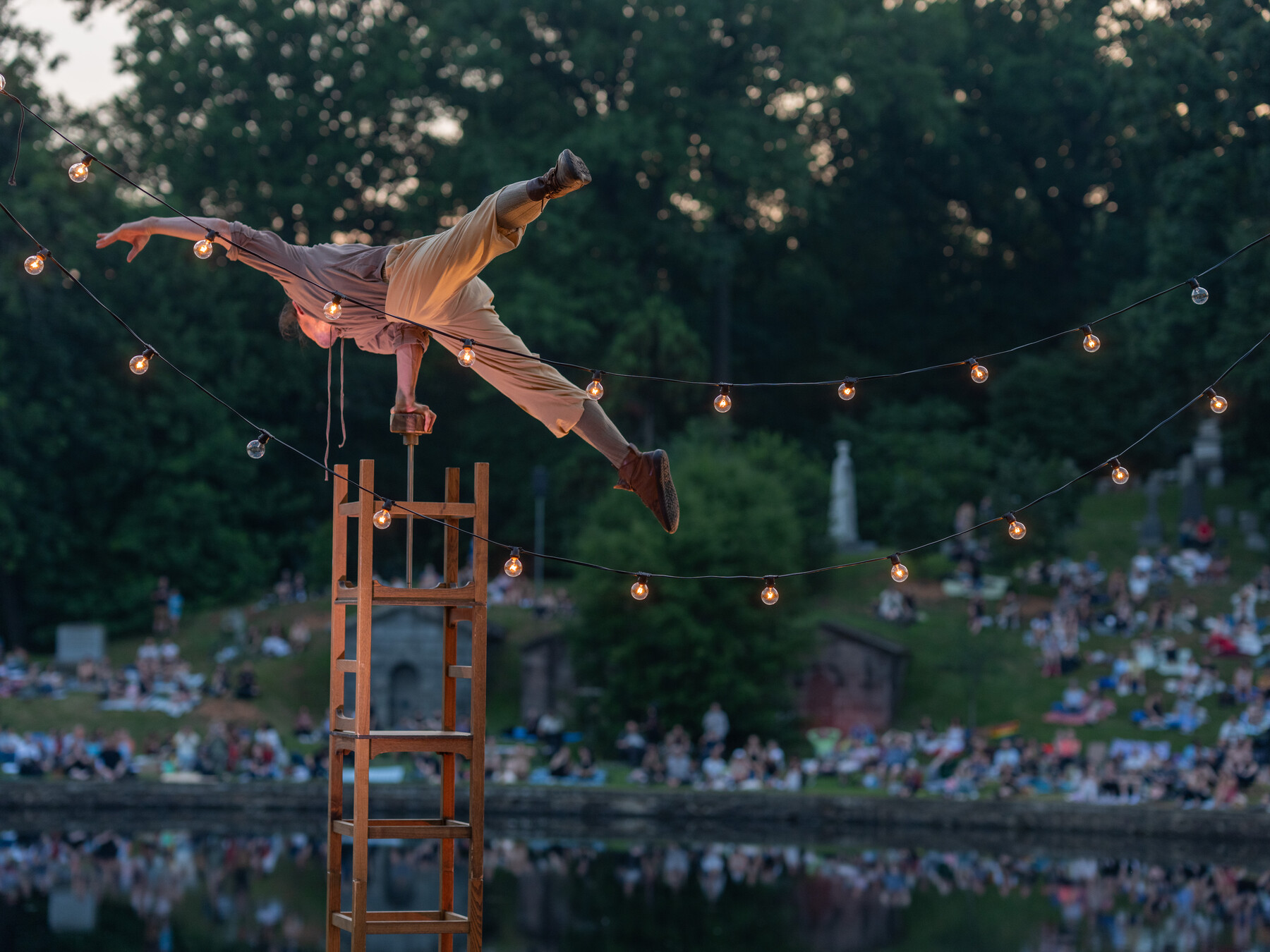 An acrobat holds a horizontal balance atop stacked chairs beside Crescent Water.