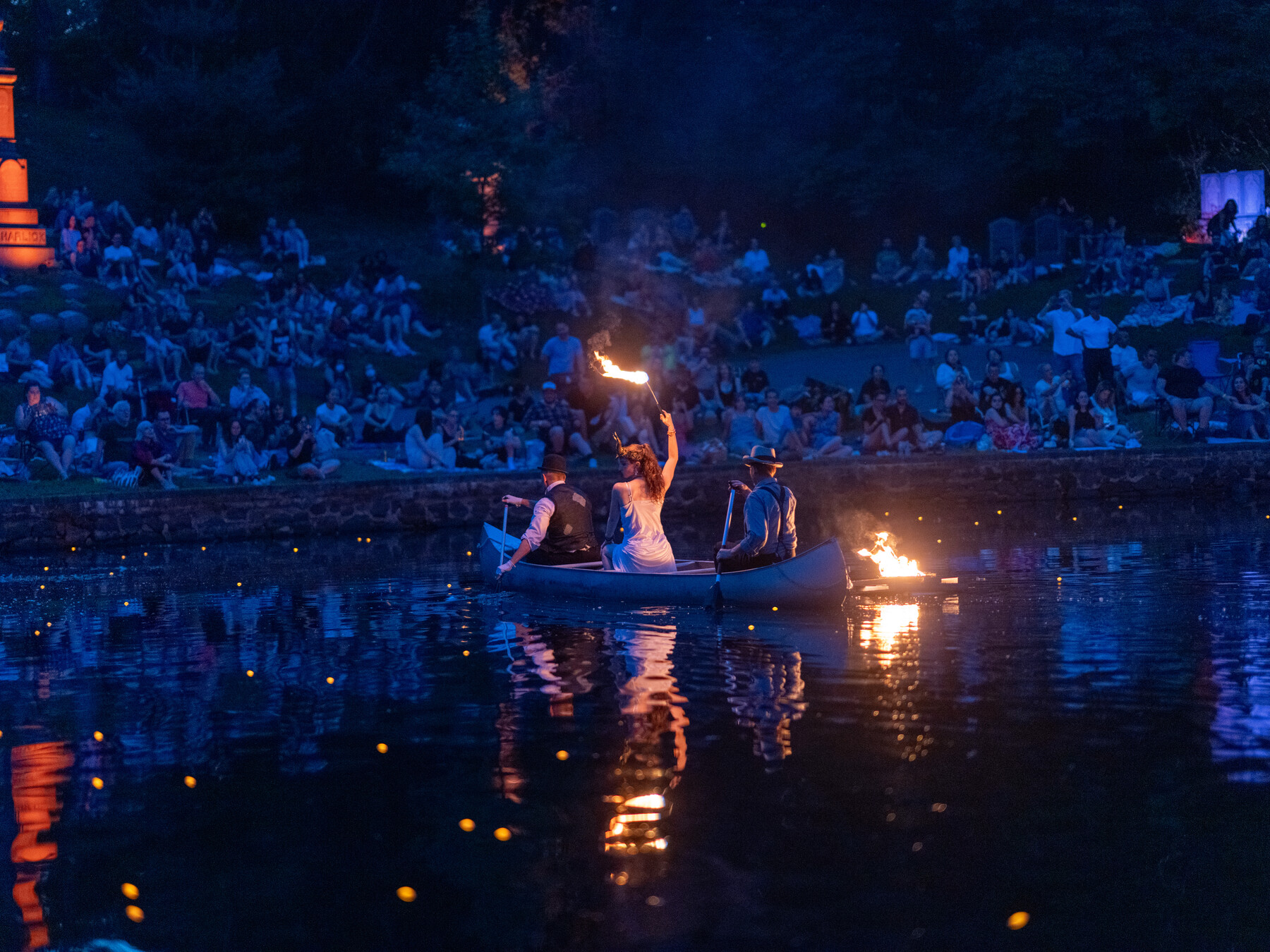 Three performers carry flaming torches in a canoe on Crescent Water after dark.