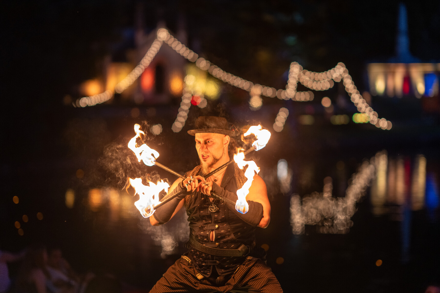 A fire performer holds bright flames against a dark evening background.