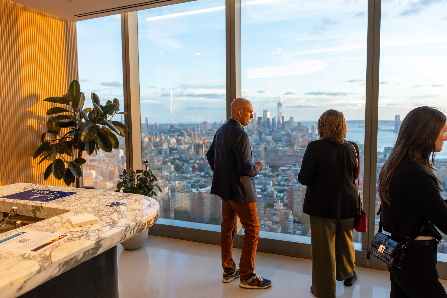 Guests talk beside windows with the New York skyline beyond.