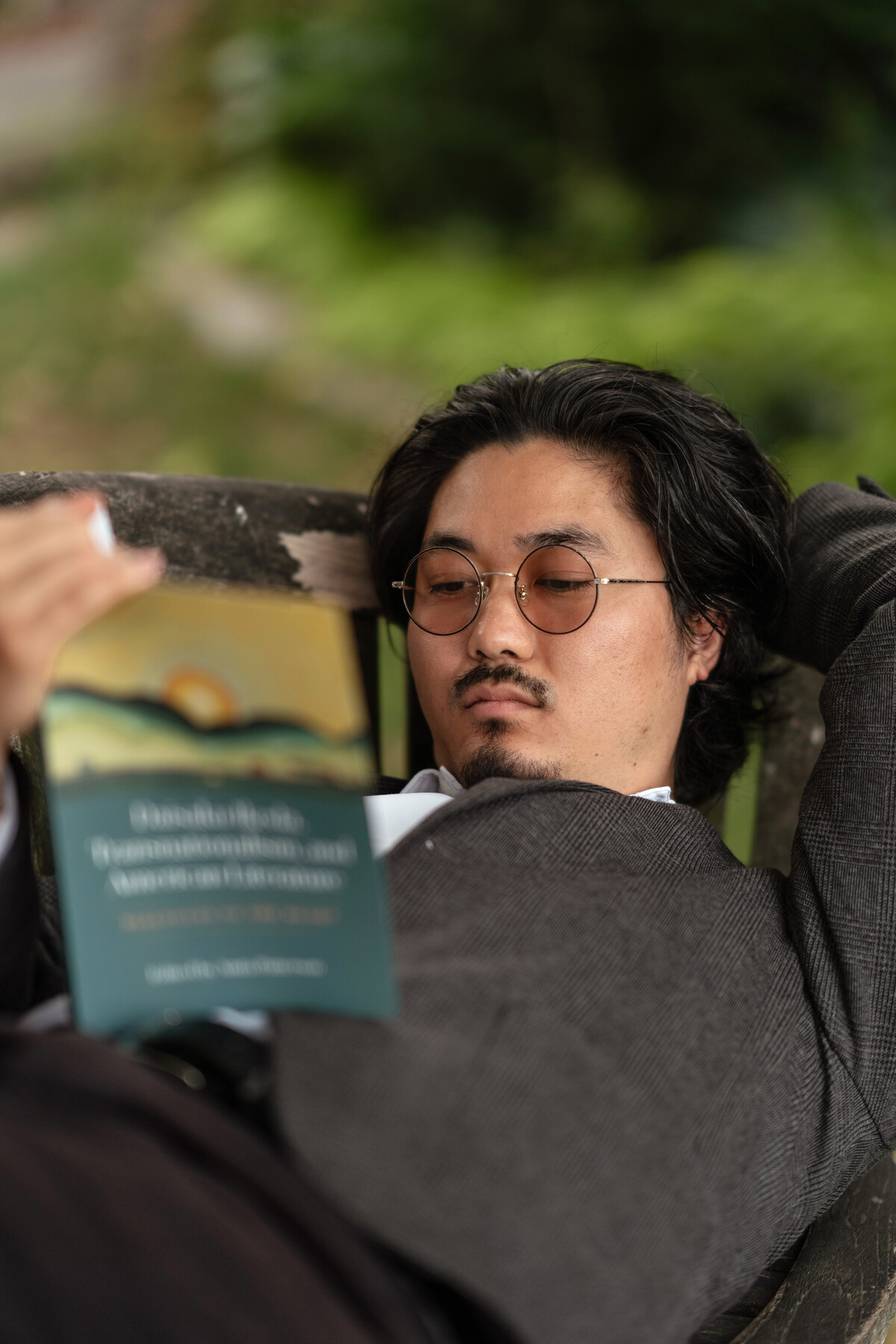 Staff member reclining on a wooden bench while reading the teal-covered book.