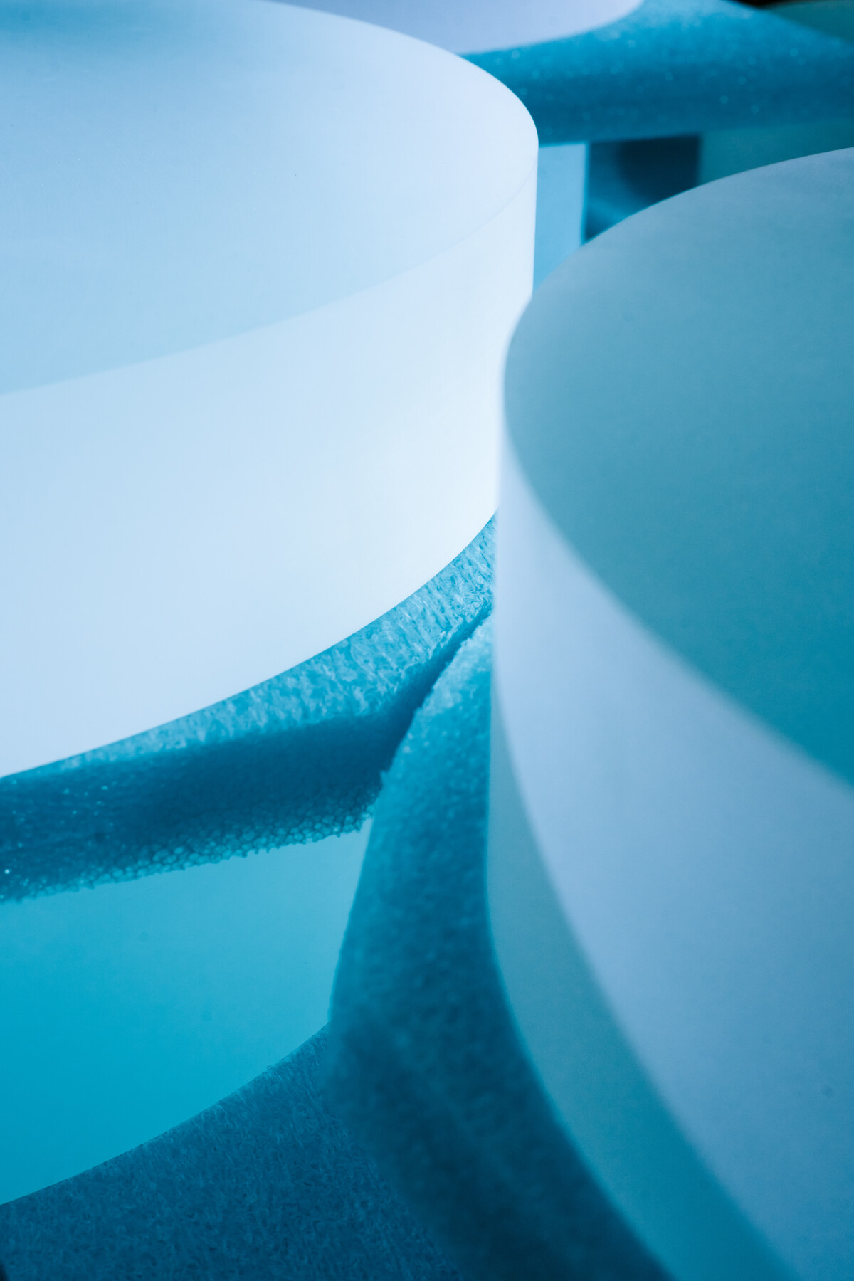 Pale curved cylinders sit in blue foam under cyan light at Optimax in Ontario, New York.