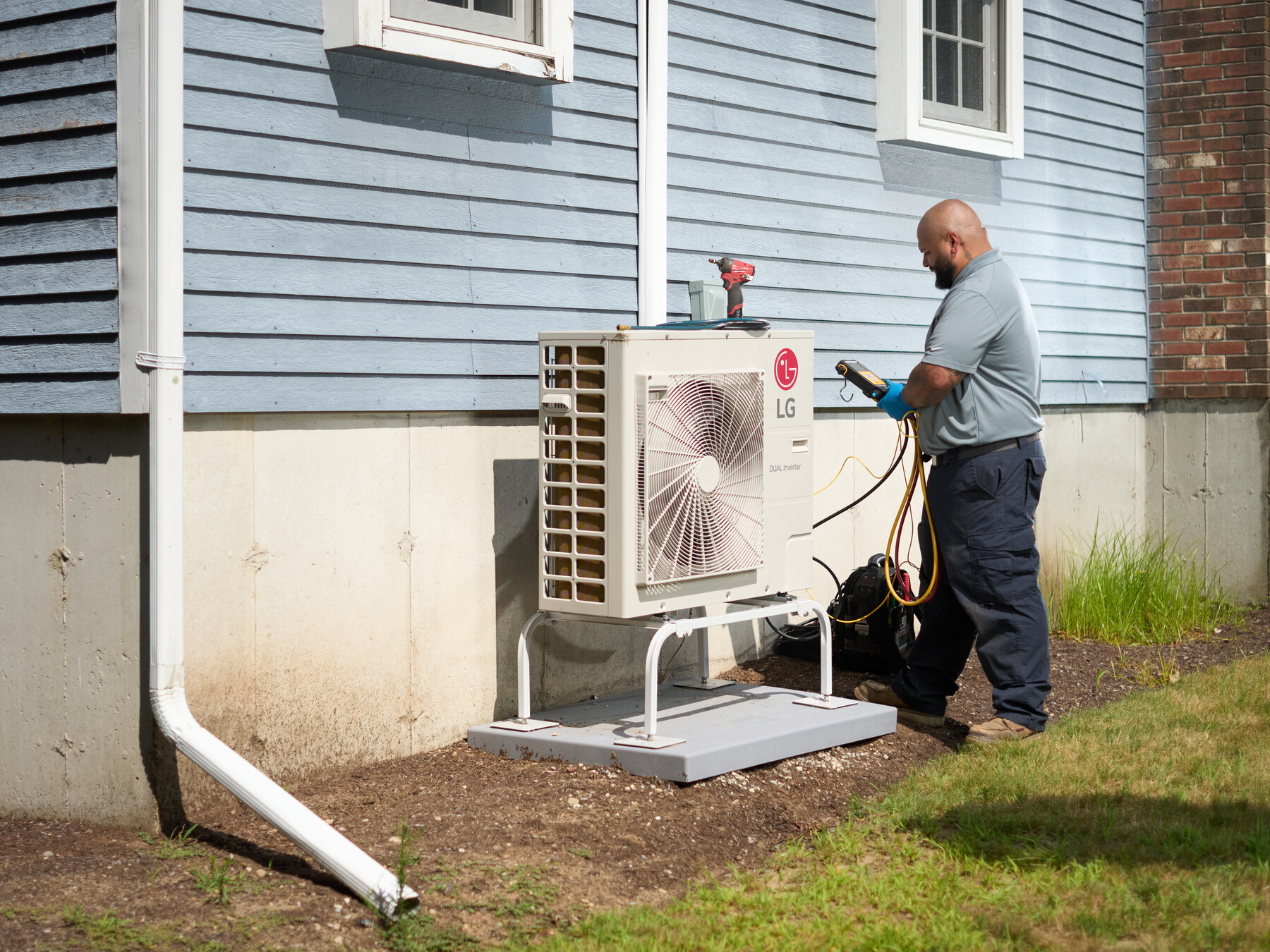 A technician stands beside an outdoor unit against a blue clapboard house.