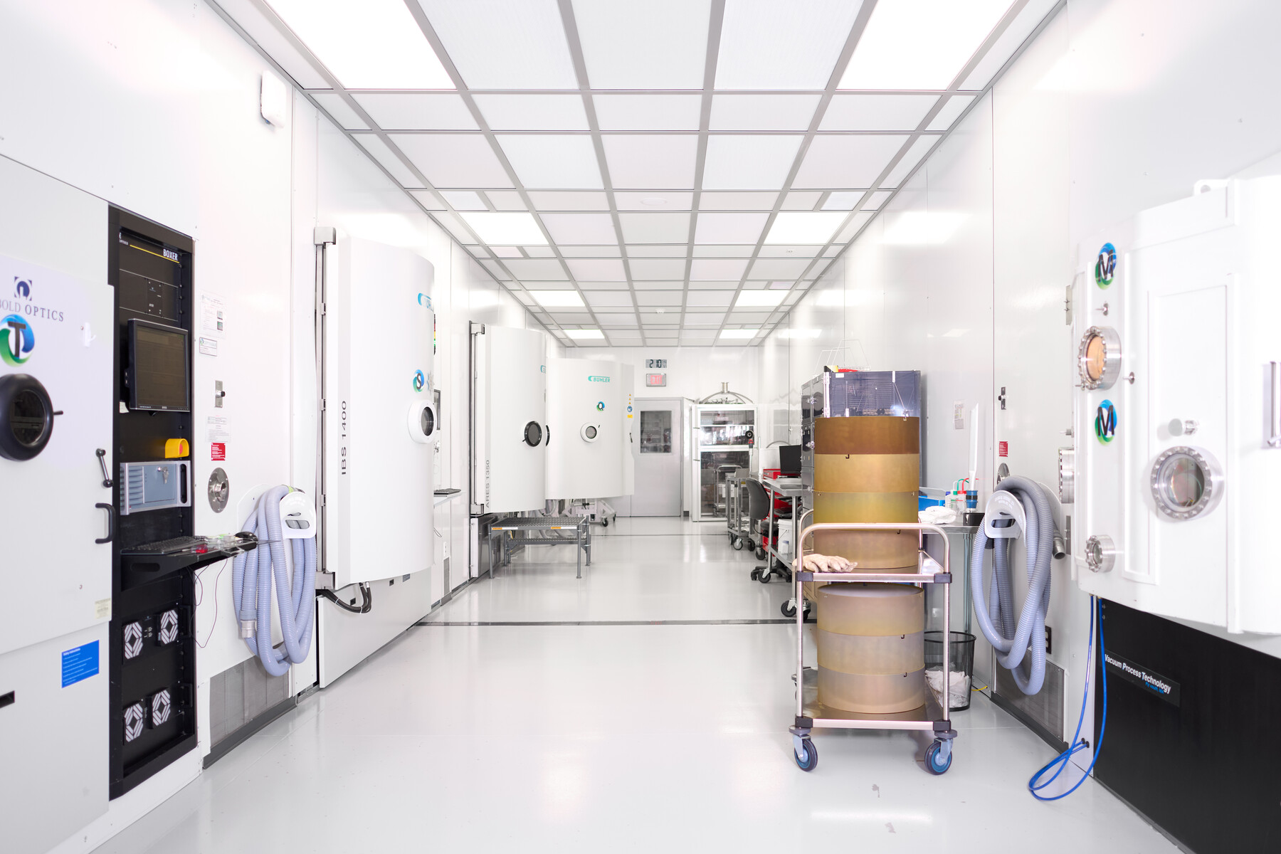 A bright white hallway lined with large equipment enclosures and wheeled carts at Optimax in Ontario, New York.
