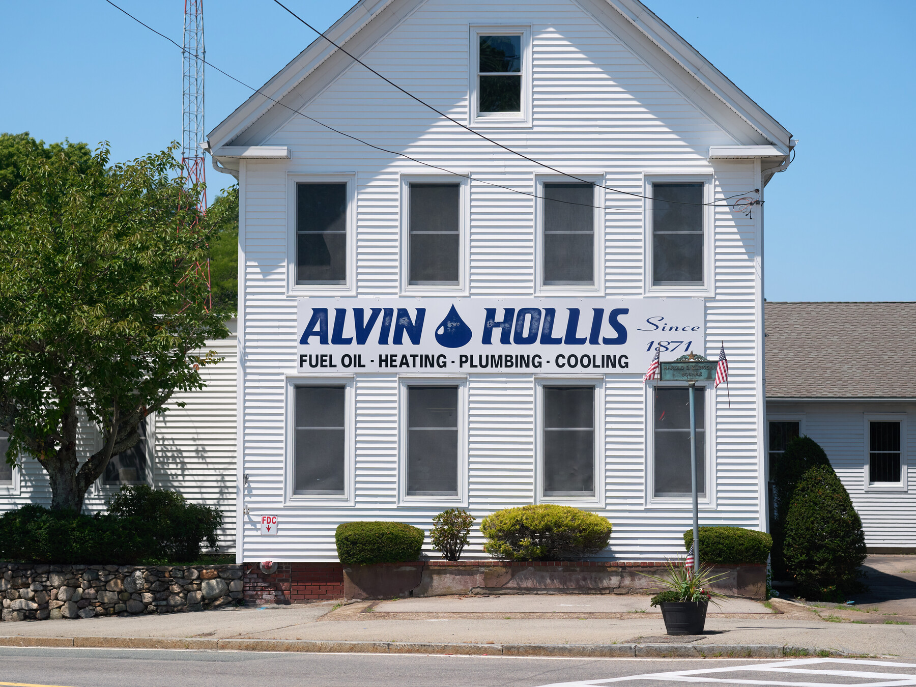 The Alvin Hollis sign spans a white clapboard building beneath a blue sky.