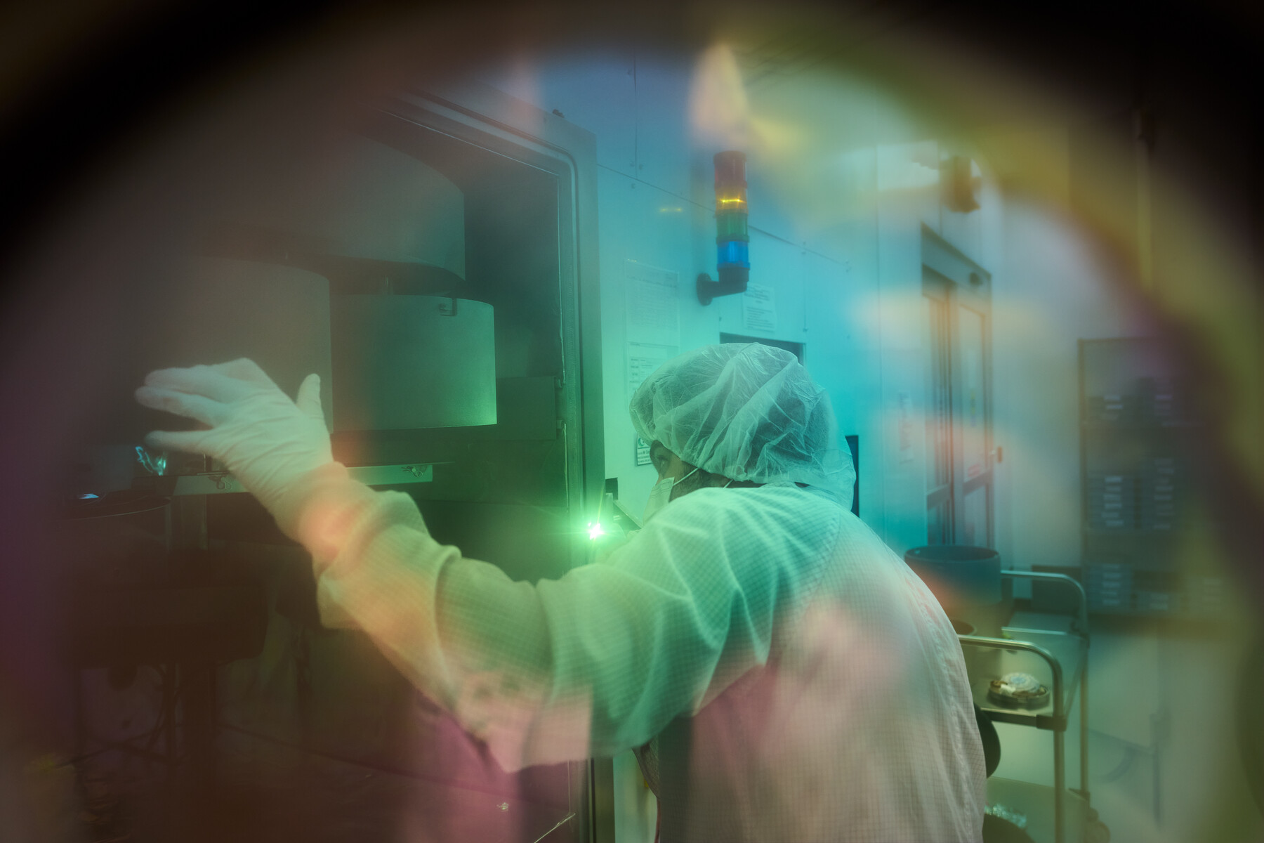 A person in protective clothing seen through a soft circular field of green, cyan and amber color at Optimax in Ontario, New York.