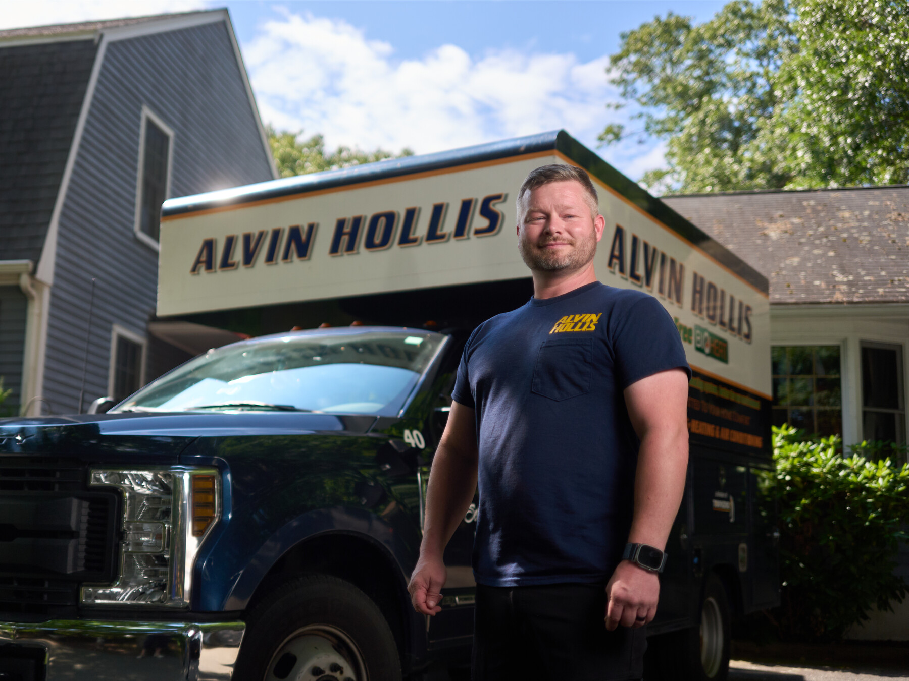 An Alvin Hollis employee poses in a navy company shirt in front of a branded service truck.
