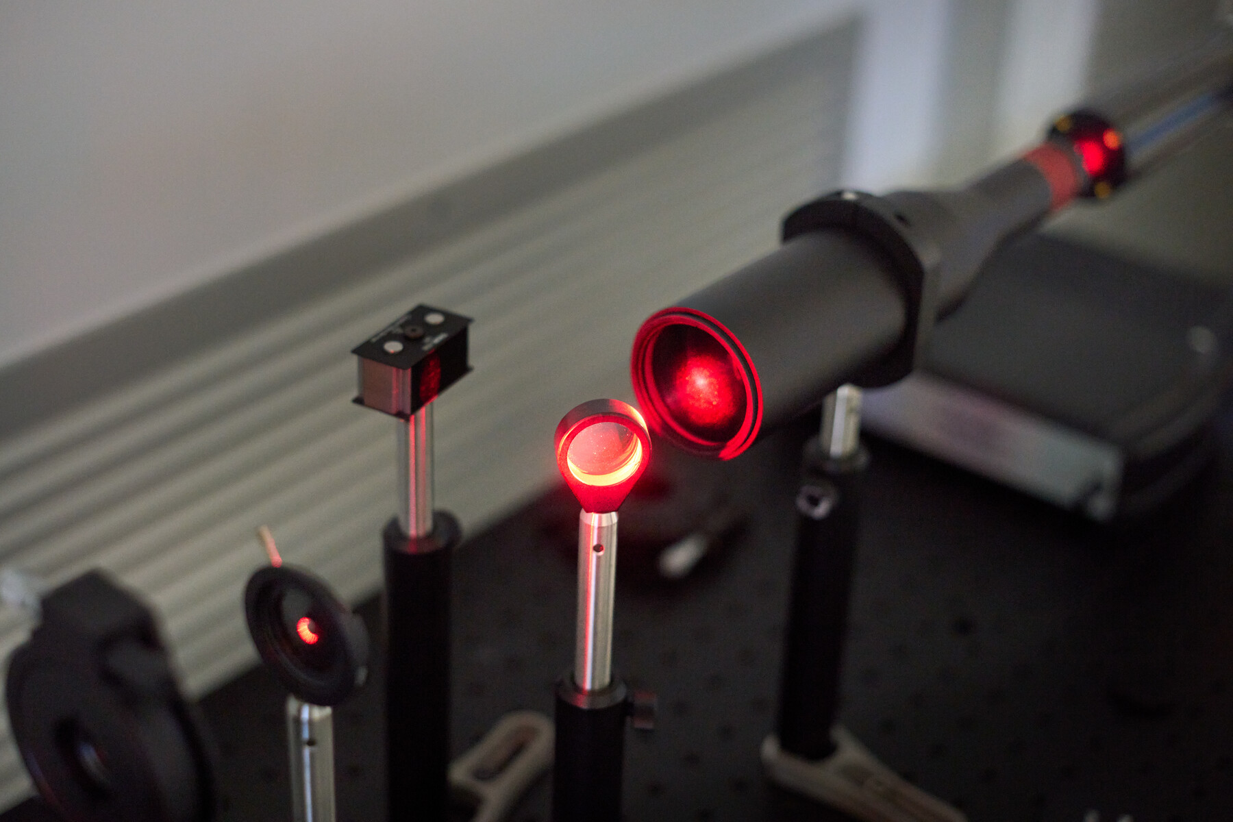 A row of mounted optical elements catches red light at Optimax in Ontario, New York.