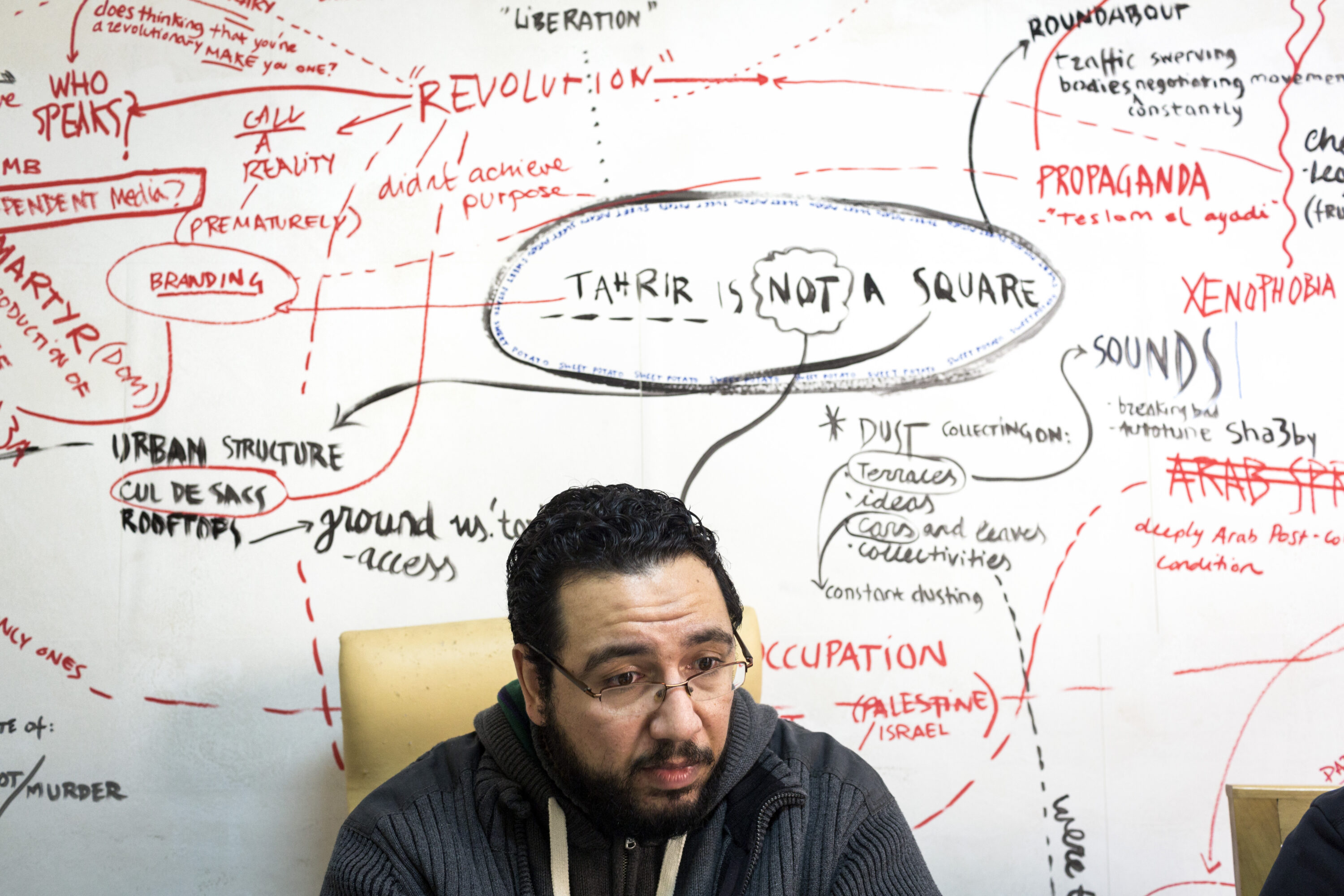 Belal Fadl seated beneath the words “Tahrir is not a square” in Mada Masr’s newsroom.