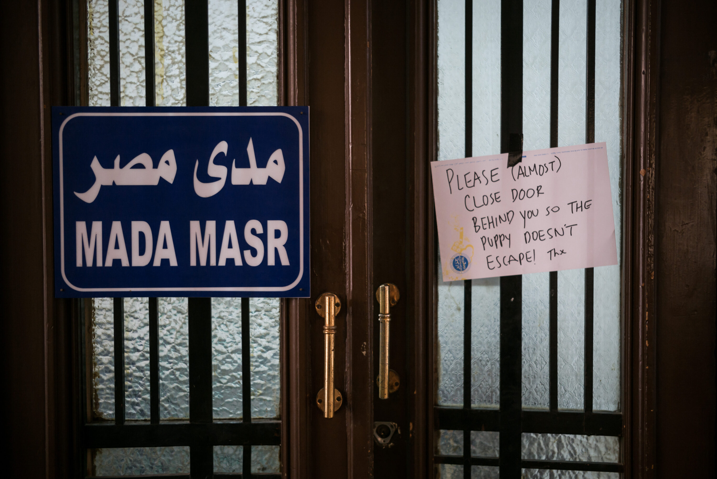 Mada Masr’s office door with its blue sign and a handwritten note about keeping the puppy inside.