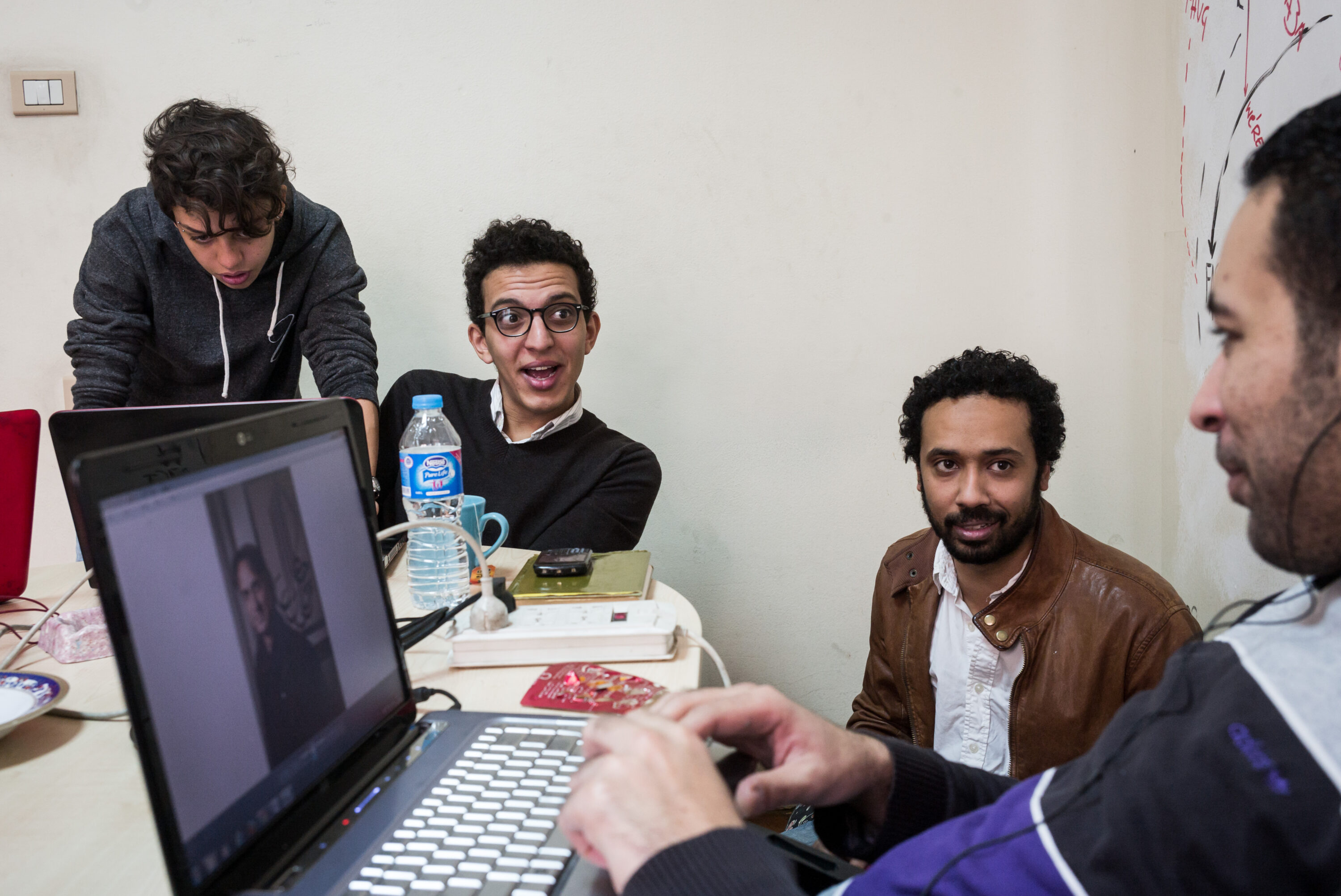 Mada Masr journalists talk around a laptop displaying a photograph in the Cairo newsroom.