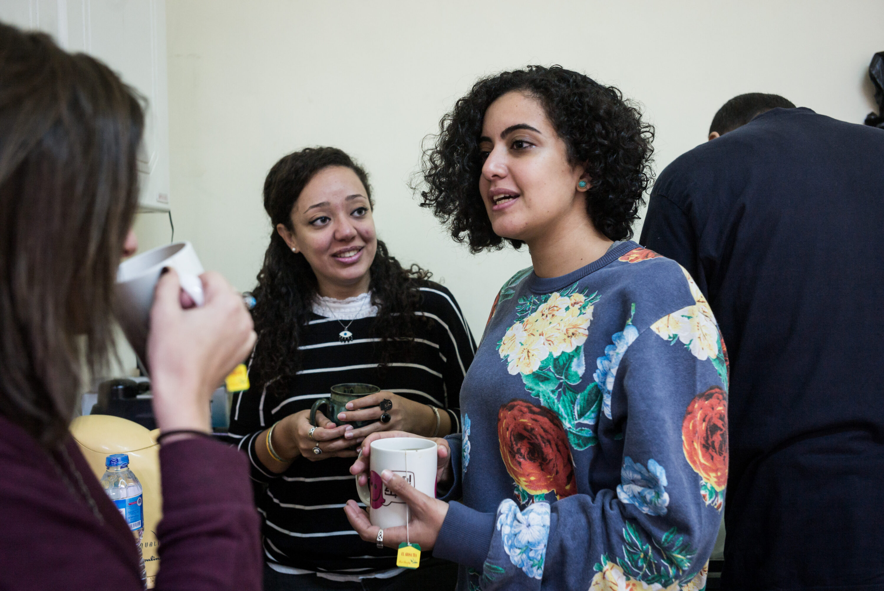 Amira Salah-Ahmed and Heba Afify hold mugs and talk with a colleague during a newsroom break.