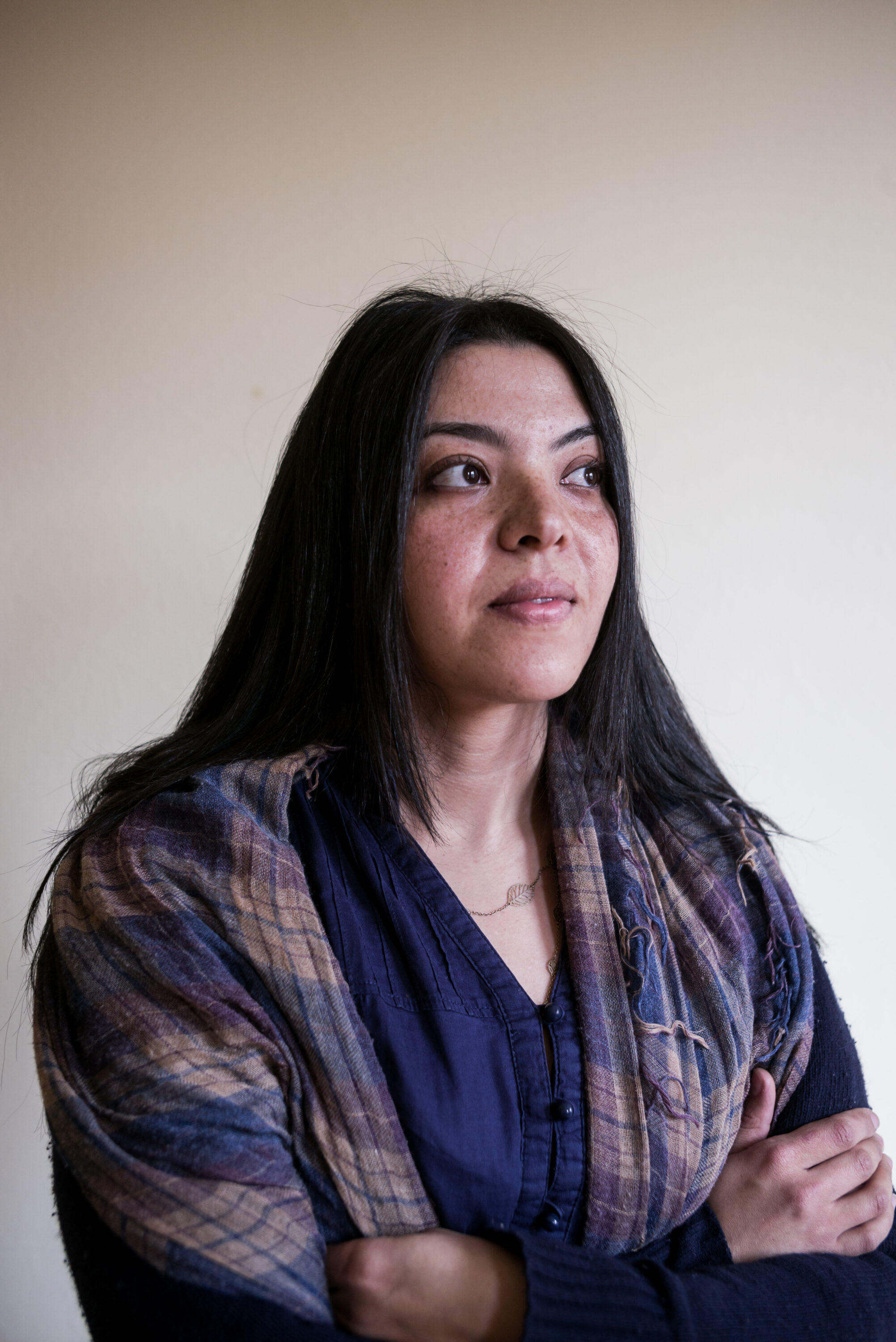 Dina K. Hussein with folded arms and a patterned scarf against a pale wall.