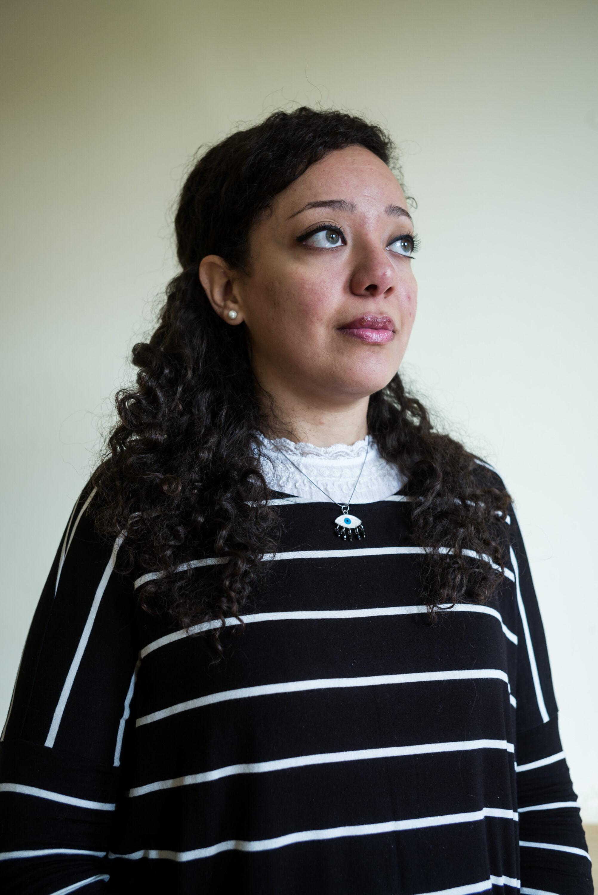 Amira Salah-Ahmed in a striped top, looking upward against a pale wall.