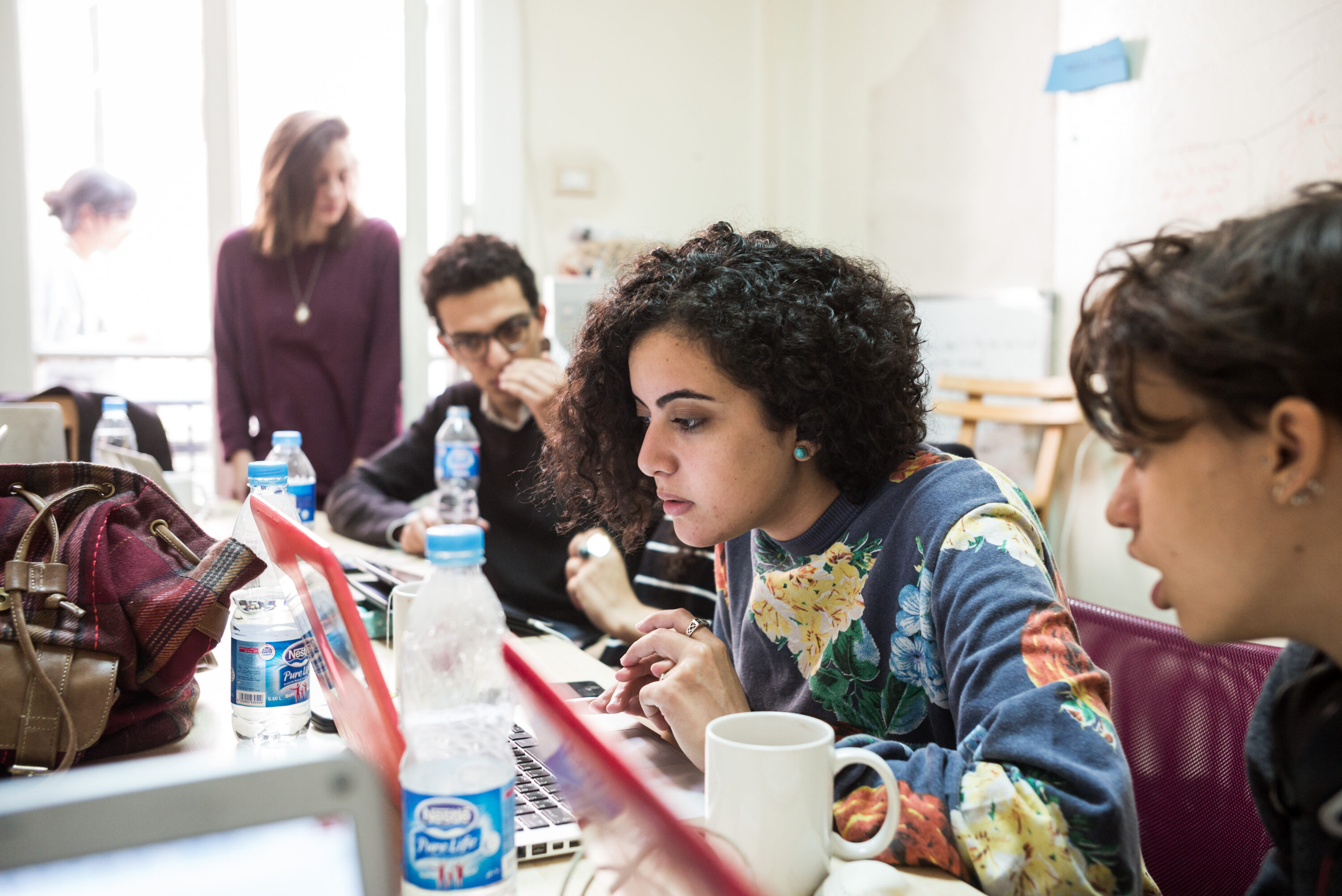 Heba Afify works at a laptop among colleagues in Mada Masr’s newsroom.