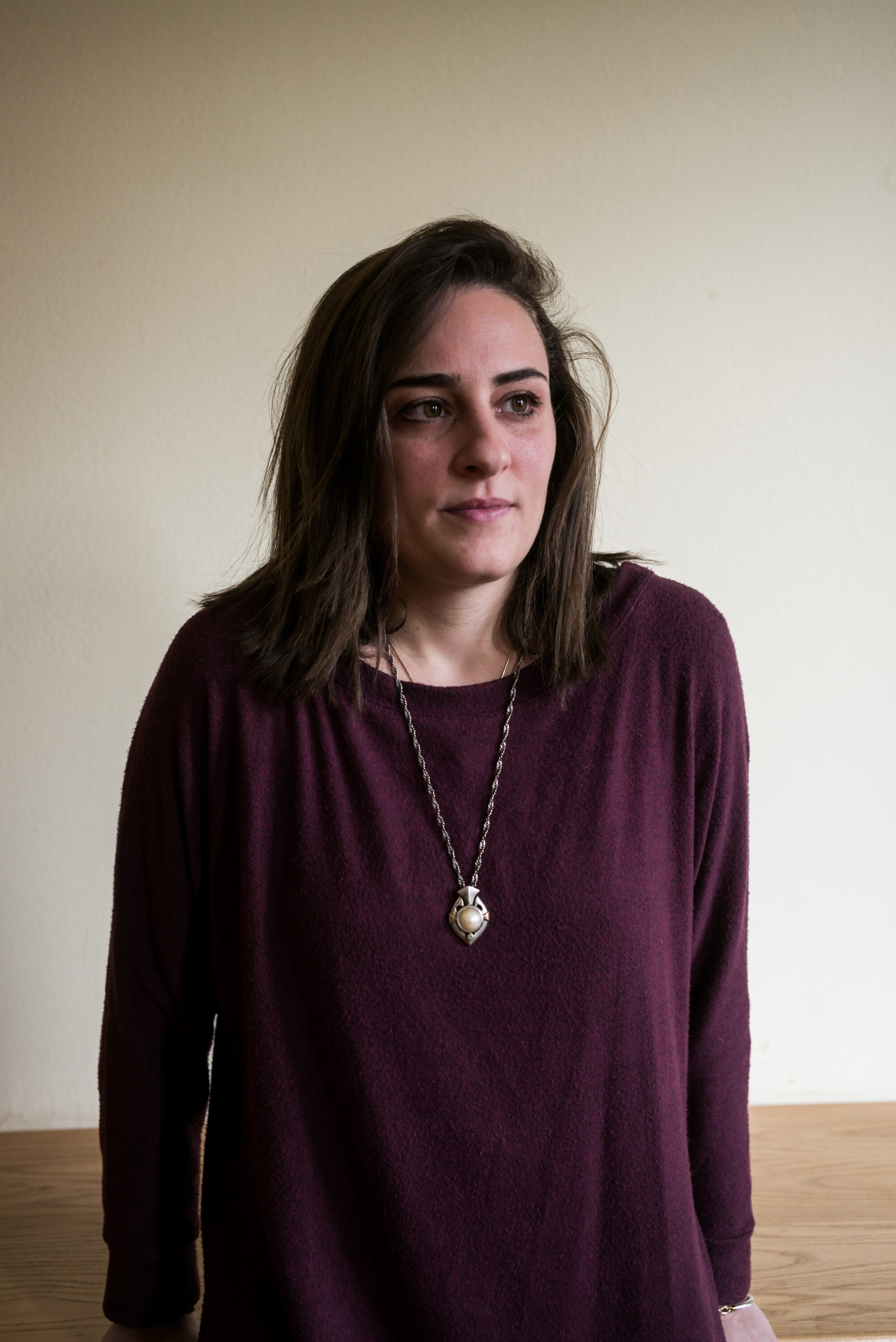 Maha ElNabawi in a burgundy sweater and long necklace against a pale wall.