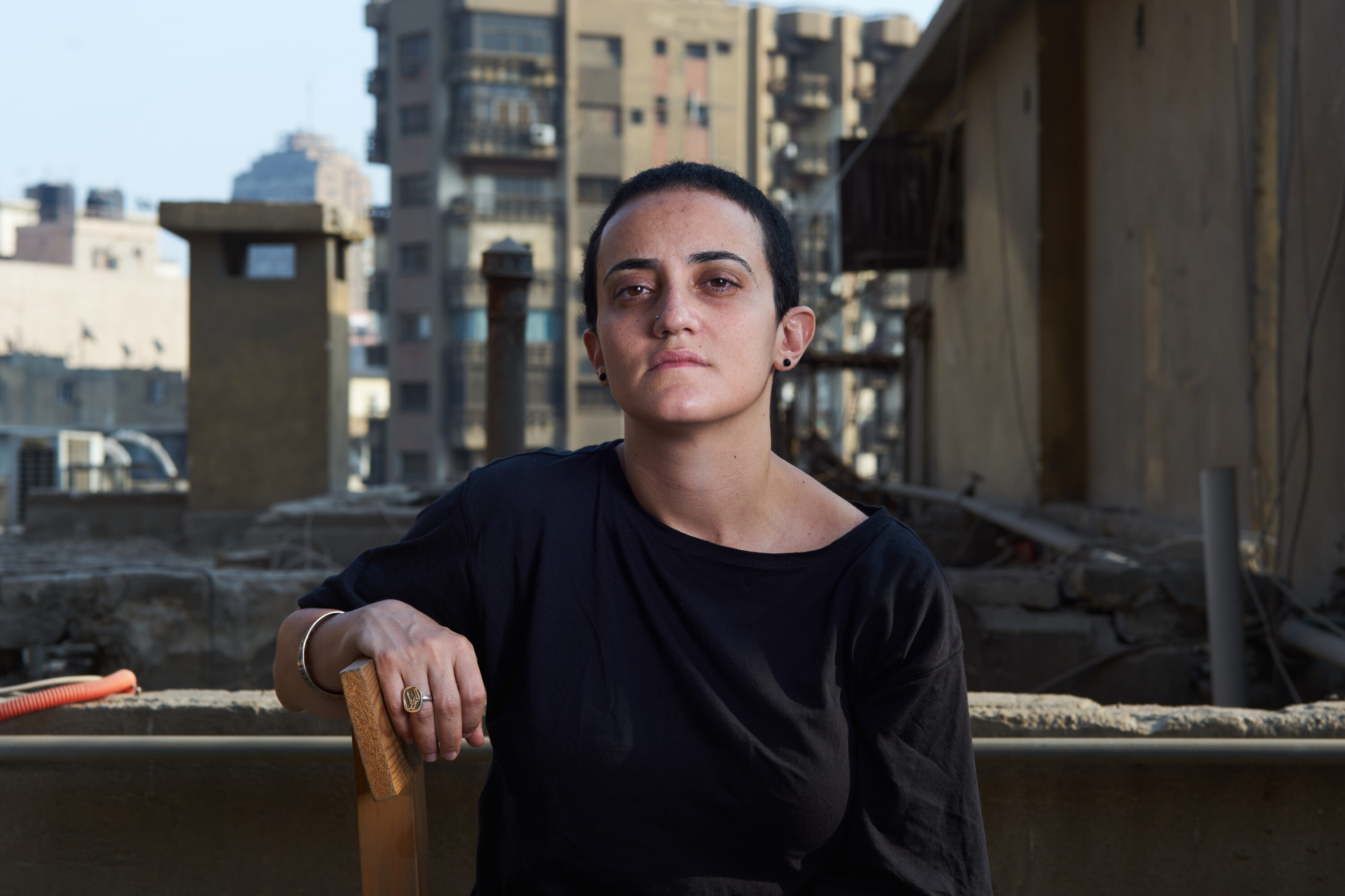 Lina Attalah seated on a Cairo rooftop, with buildings behind her.