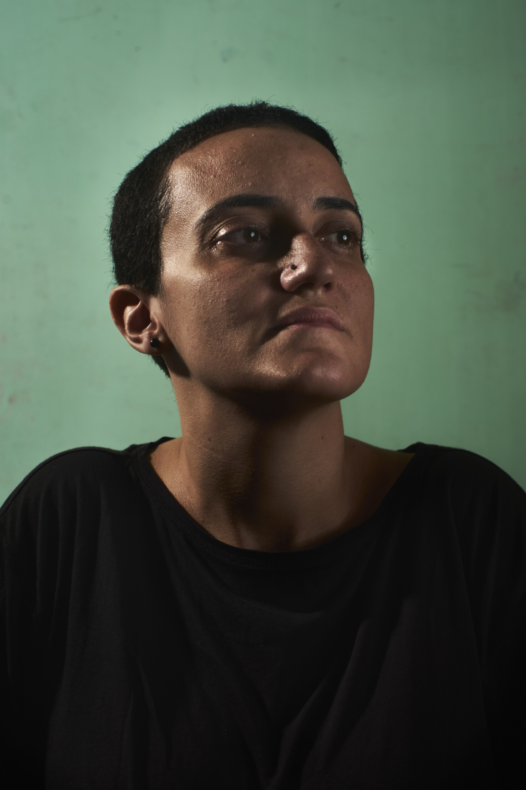 Lina Attalah against a green wall, looking to one side.