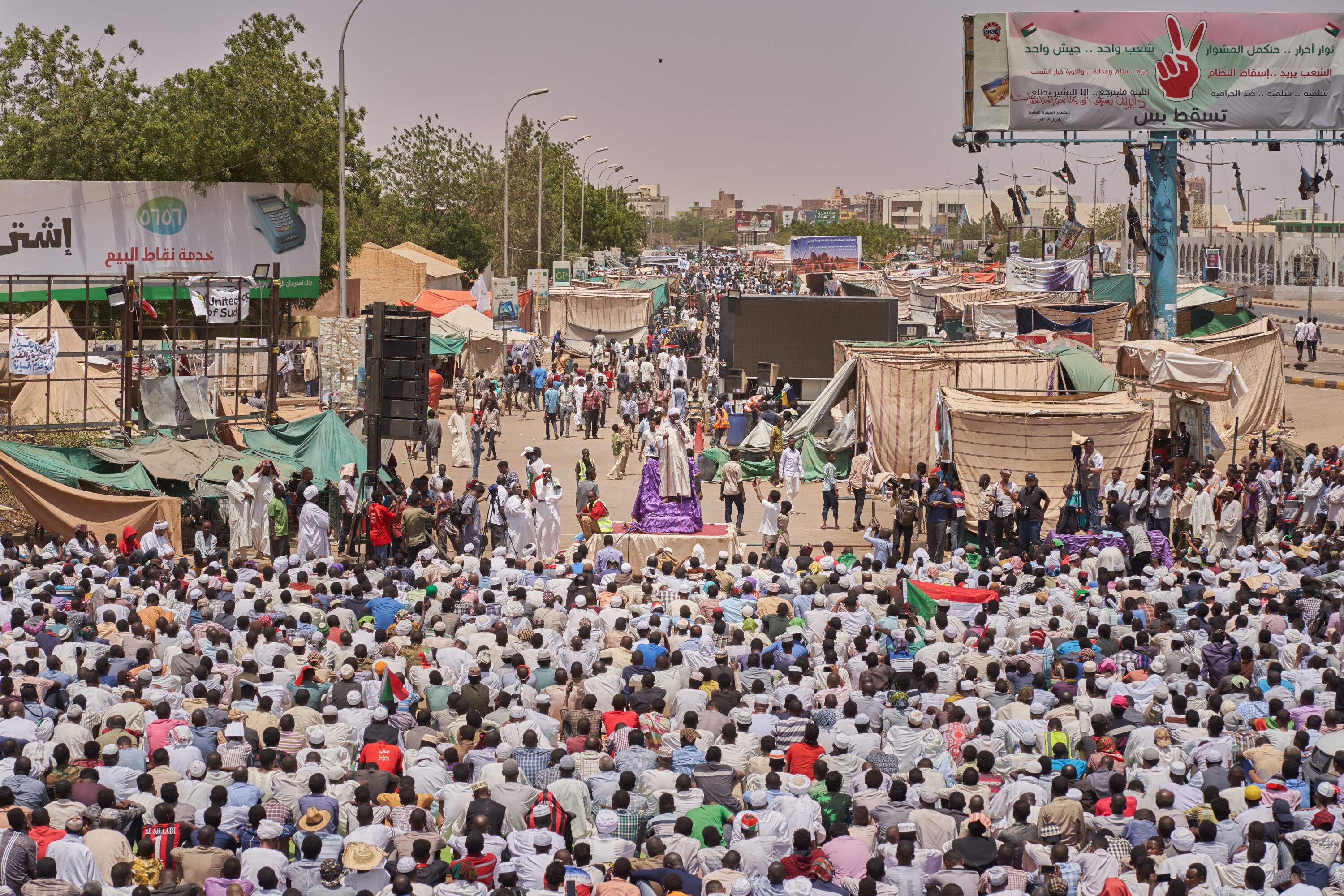 A large seated crowd fills a street lined with tents, banners and loudspeakers at the Khartoum sit-in.