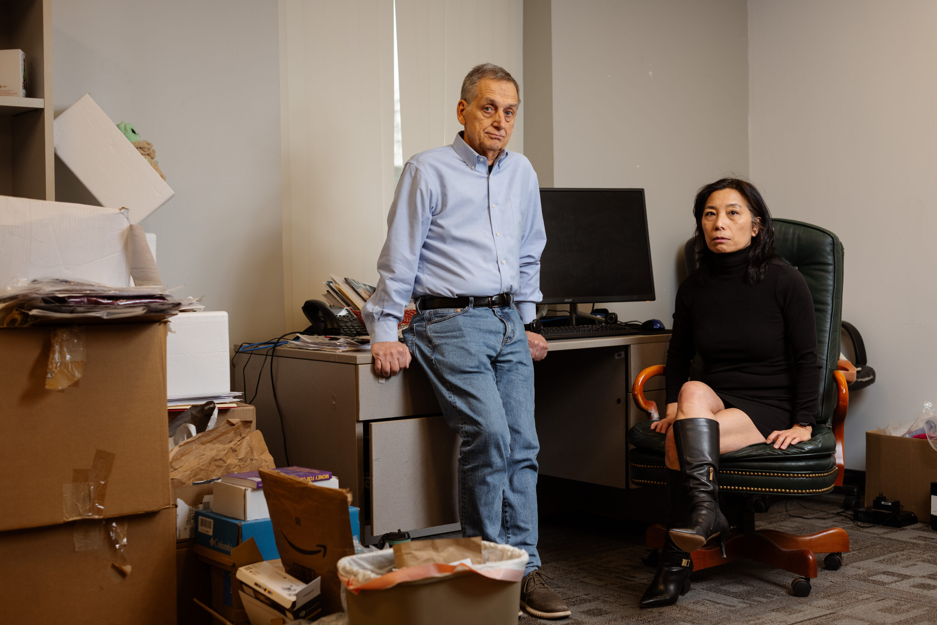 Bill Keefe and Juli Lee pose beside an office desk surrounded by papers and open cartons.