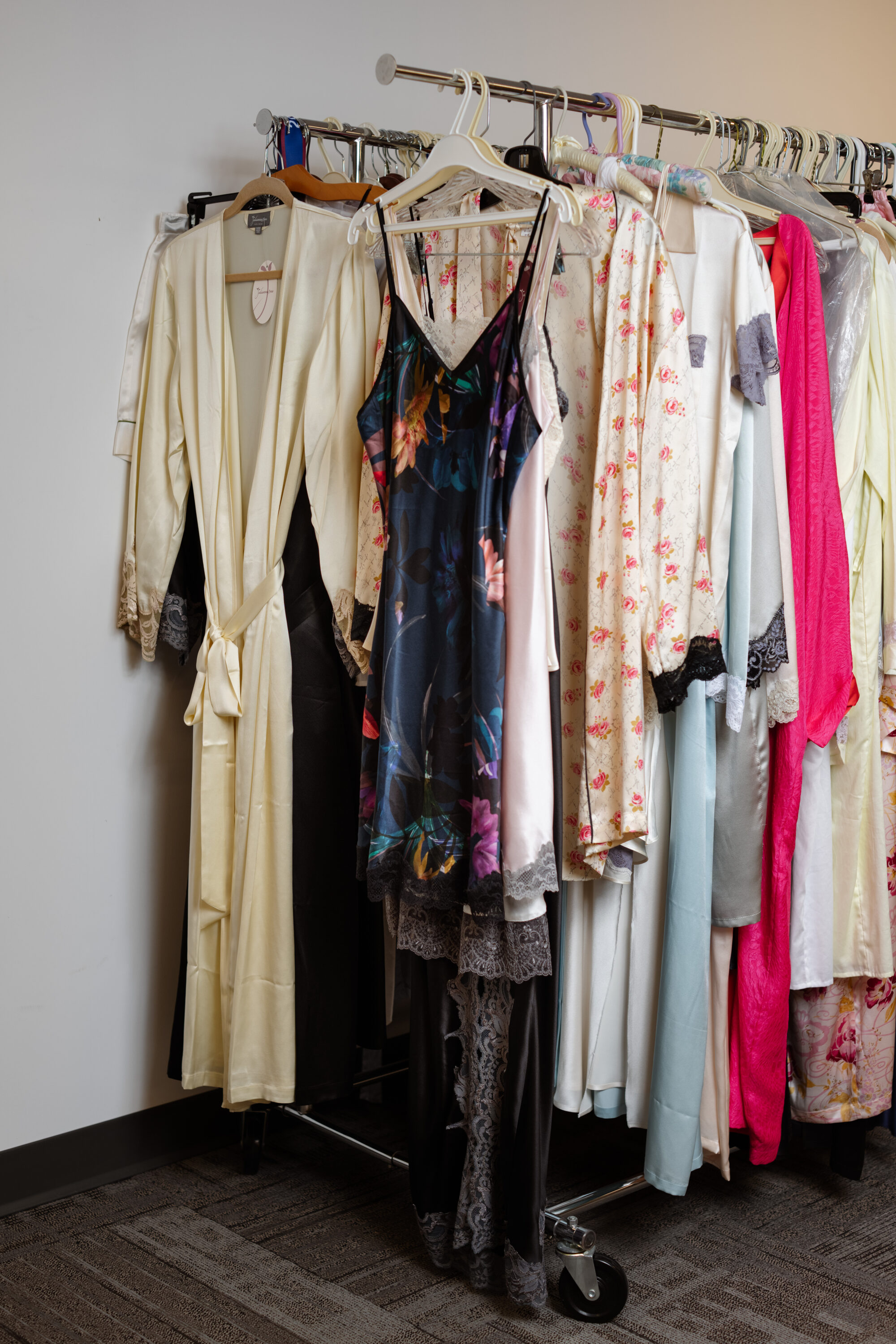 Robes and sleepwear in cream, floral, blue and pink fabrics hang on a rolling rack.