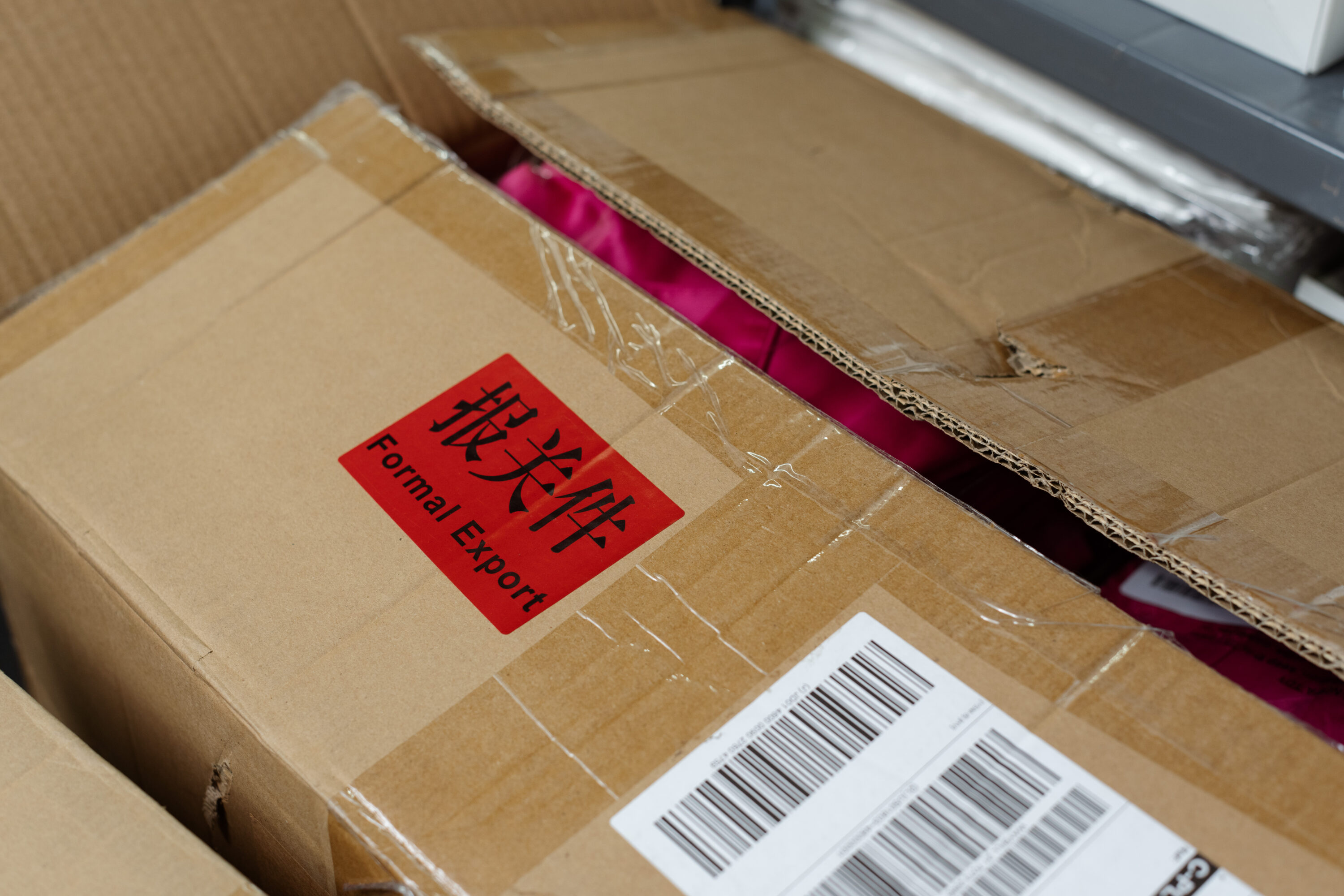 A red Formal Export label is attached to an open carton containing pink fabric.