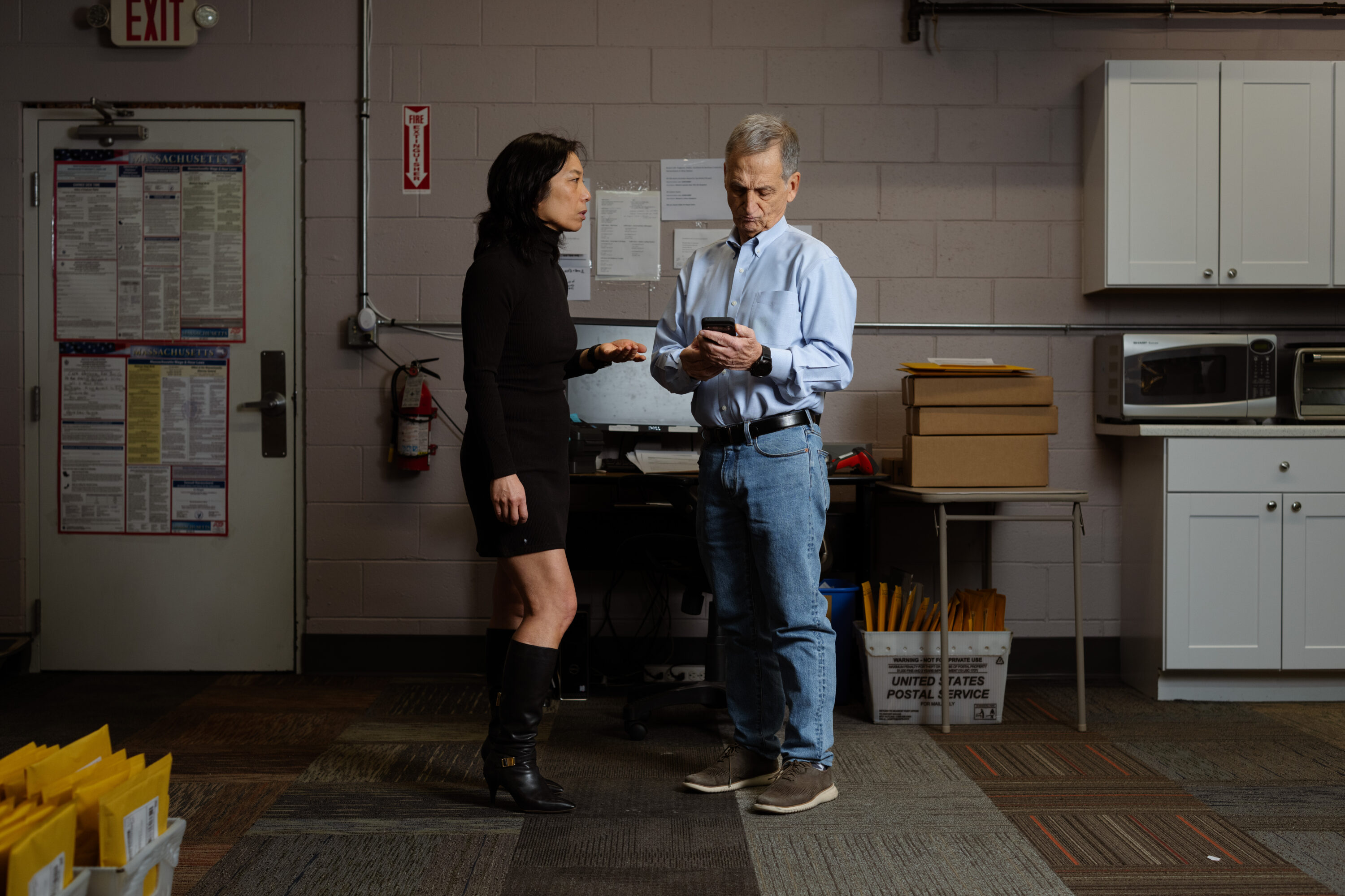 Juli Lee gestures beside Bill Keefe as he looks at a phone in the back workspace.